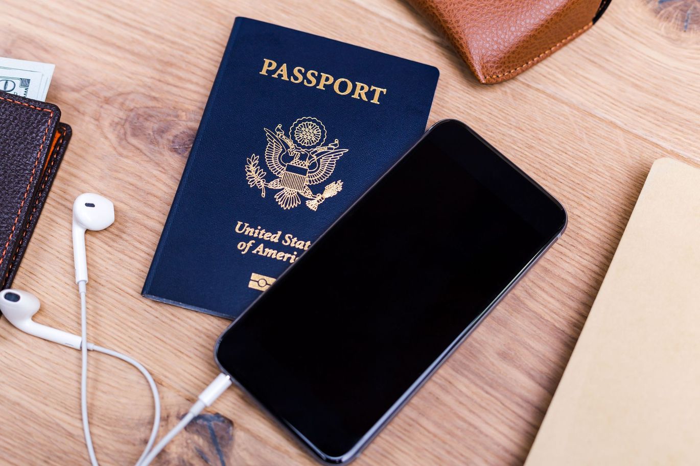 Pasaporte, teléfono, auriculares y billetera sobre una superficie de madera, lo que sugiere preparativos de viaje.
