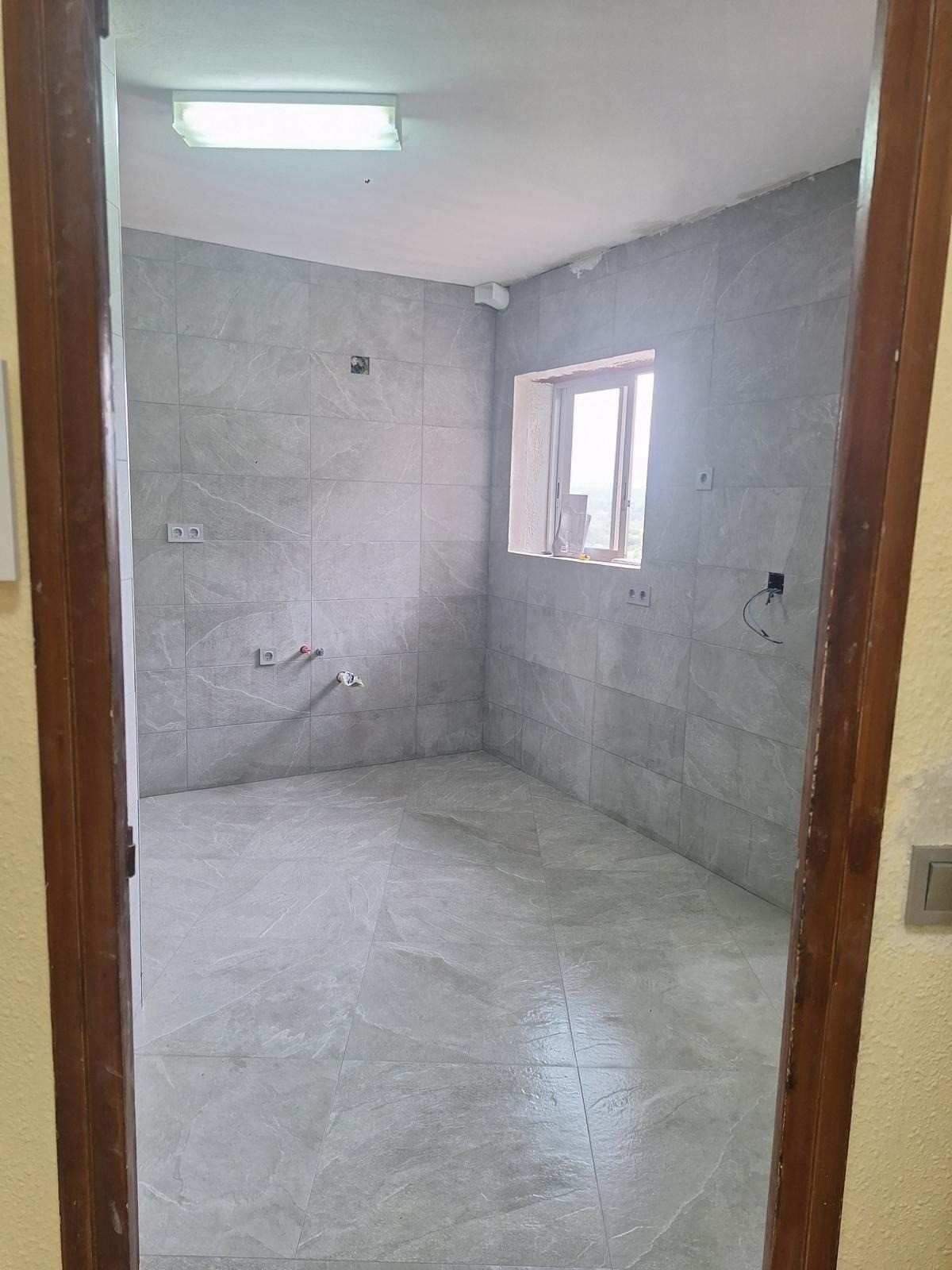 Baño vacío alicatado en construcción con ventana y luz de techo.