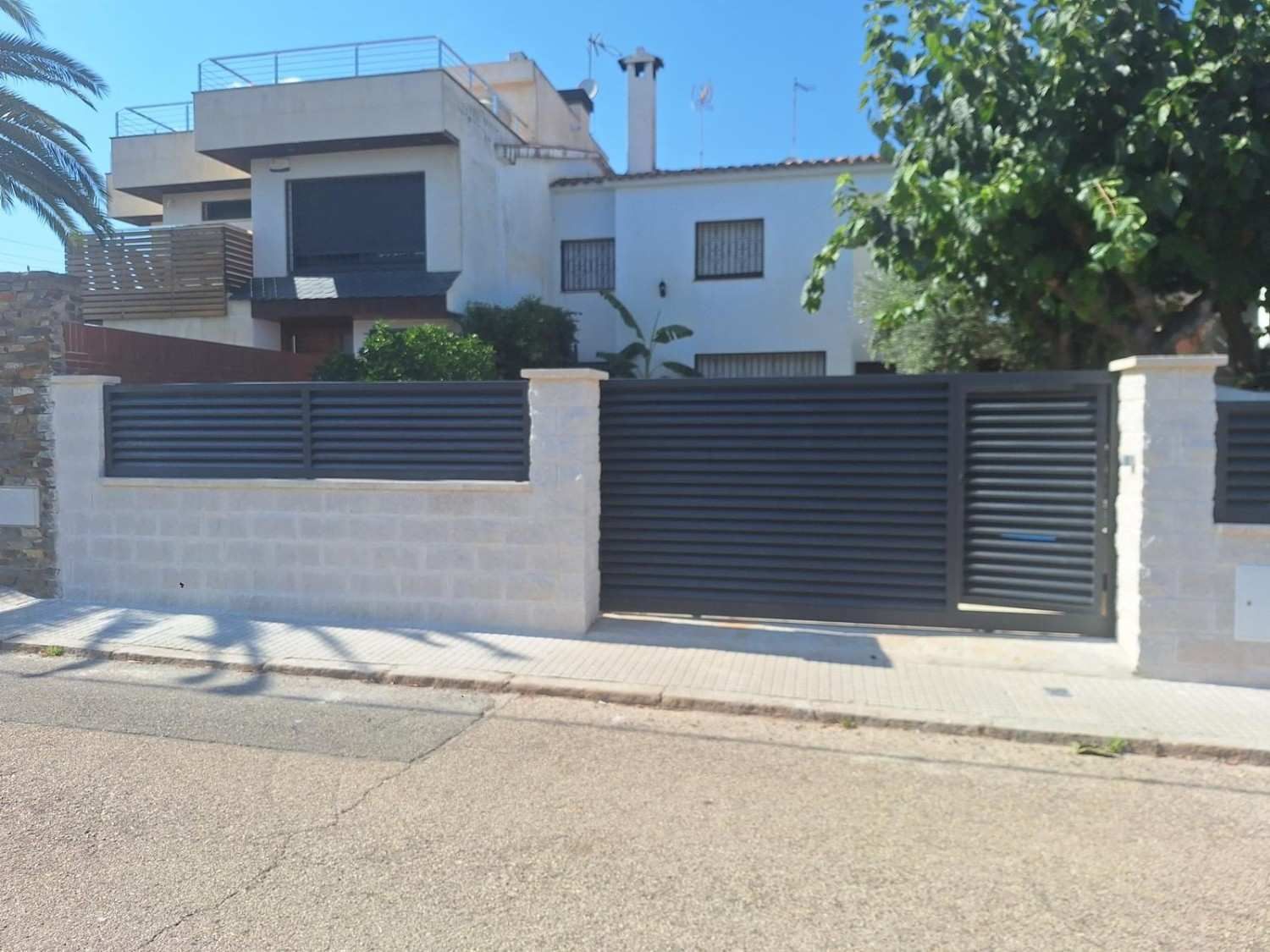 Moderna casa blanca de dos plantas con puerta negra y muro bajo de ladrillo en una calle tranquila.