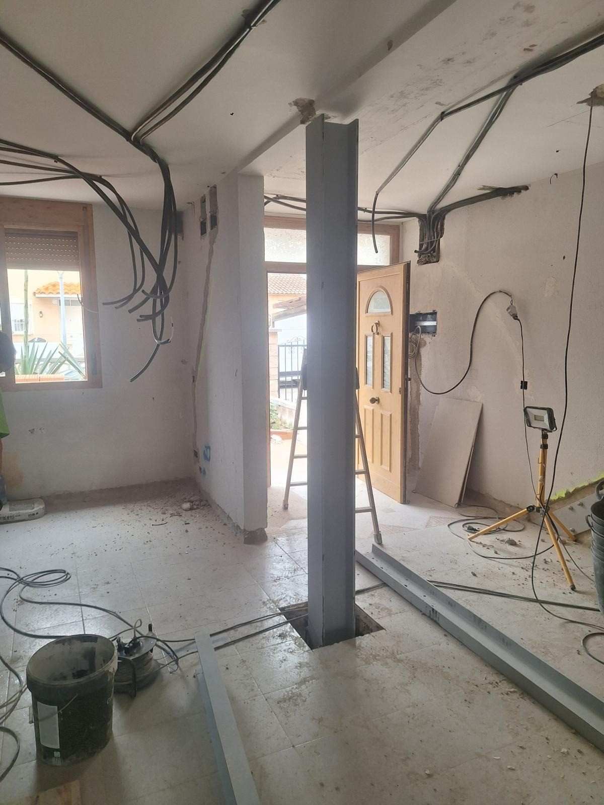 Habitación parcialmente reformada con cableado a la vista, una columna de soporte central, escombros y una puerta abierta.