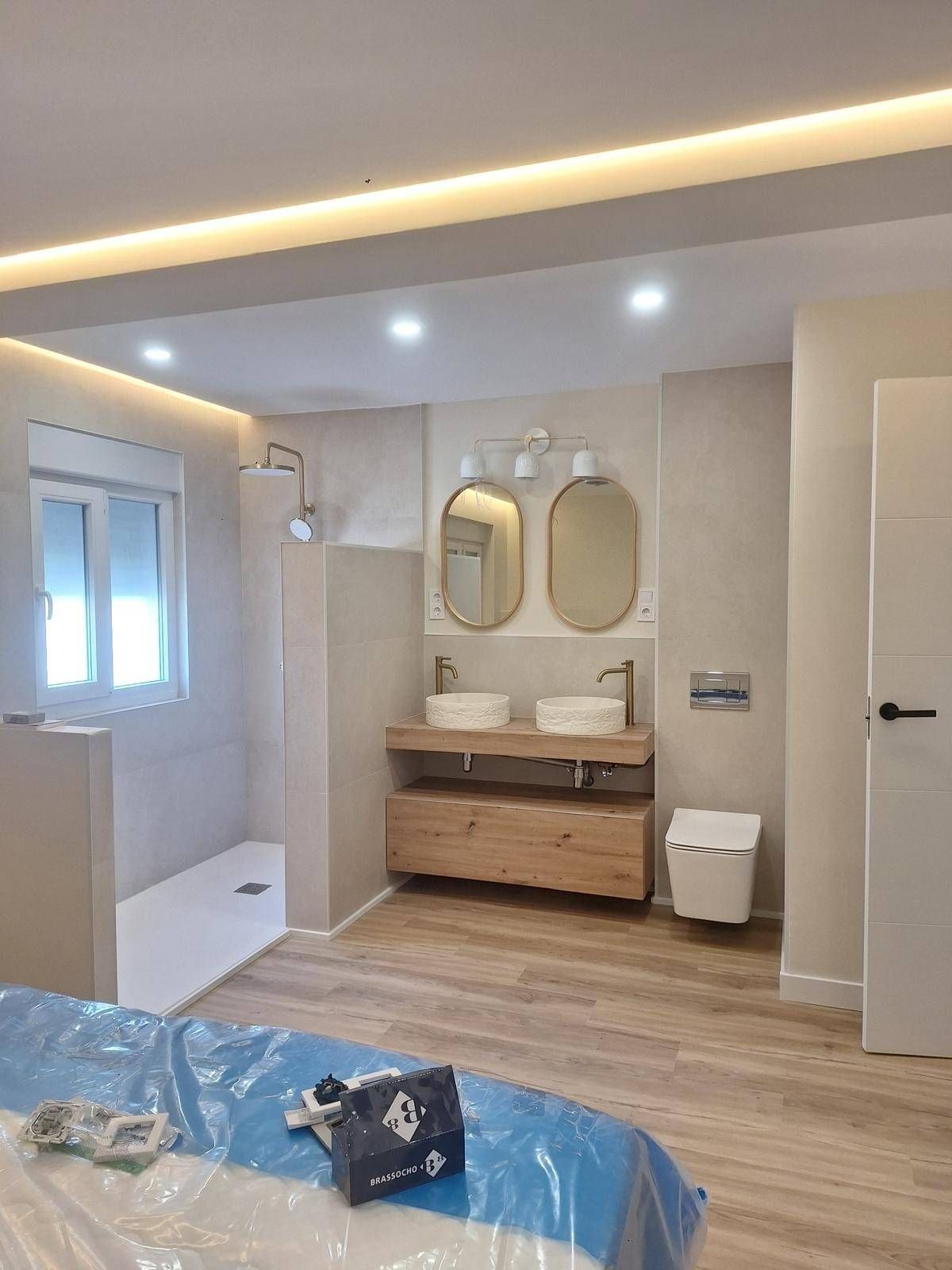 Baño moderno con tocador de madera, dos espejos, ducha a ras de suelo y bañera junto a la ventana.
