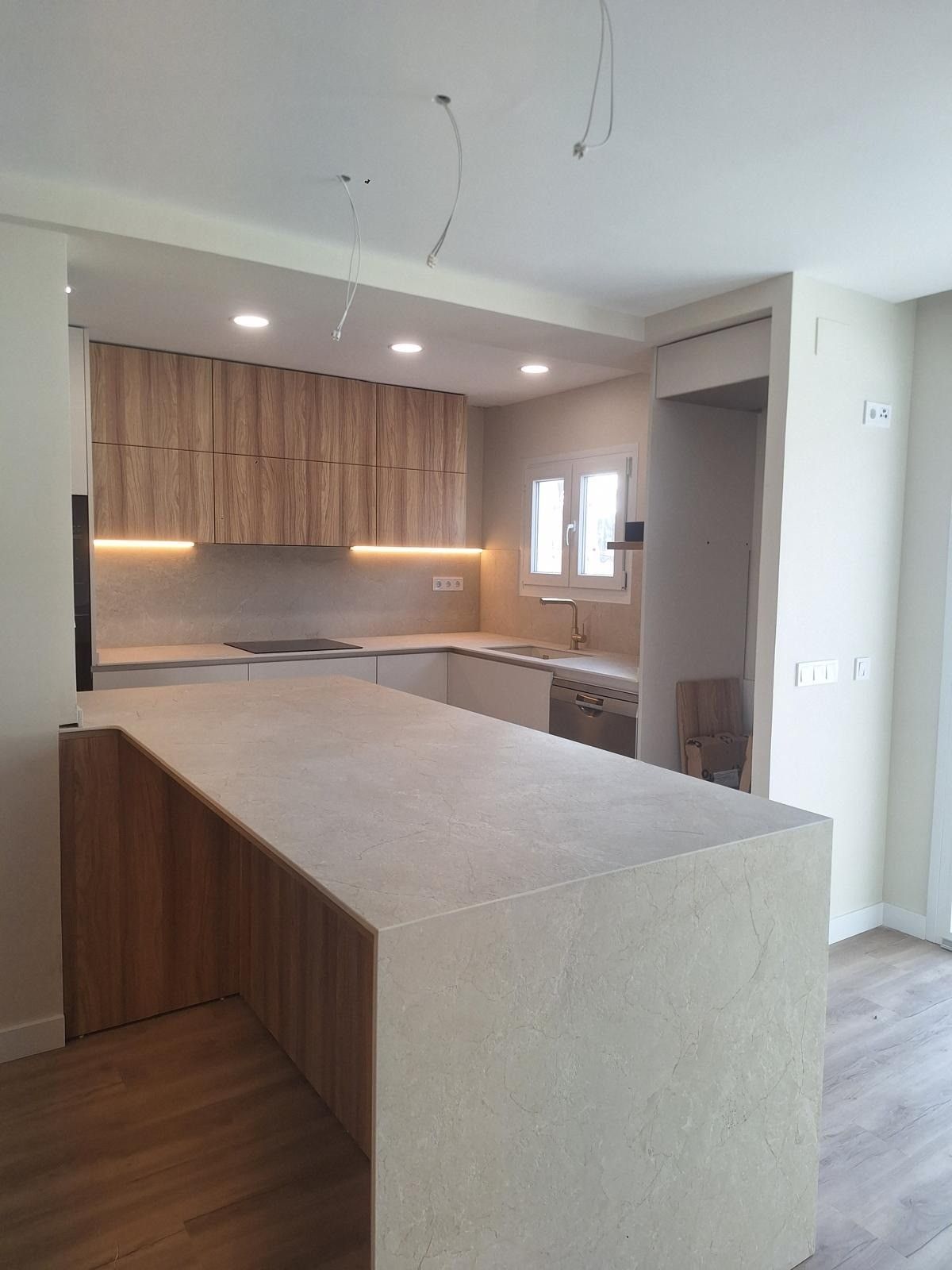 Cocina moderna con gabinetes de madera clara, encimeras beige y una isla tipo península con iluminación empotrada.