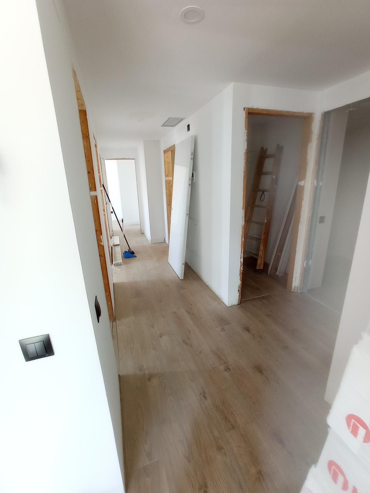 Pasillo luminoso en una casa sin amueblar con paredes blancas, suelos de madera clara y puertas abiertas.