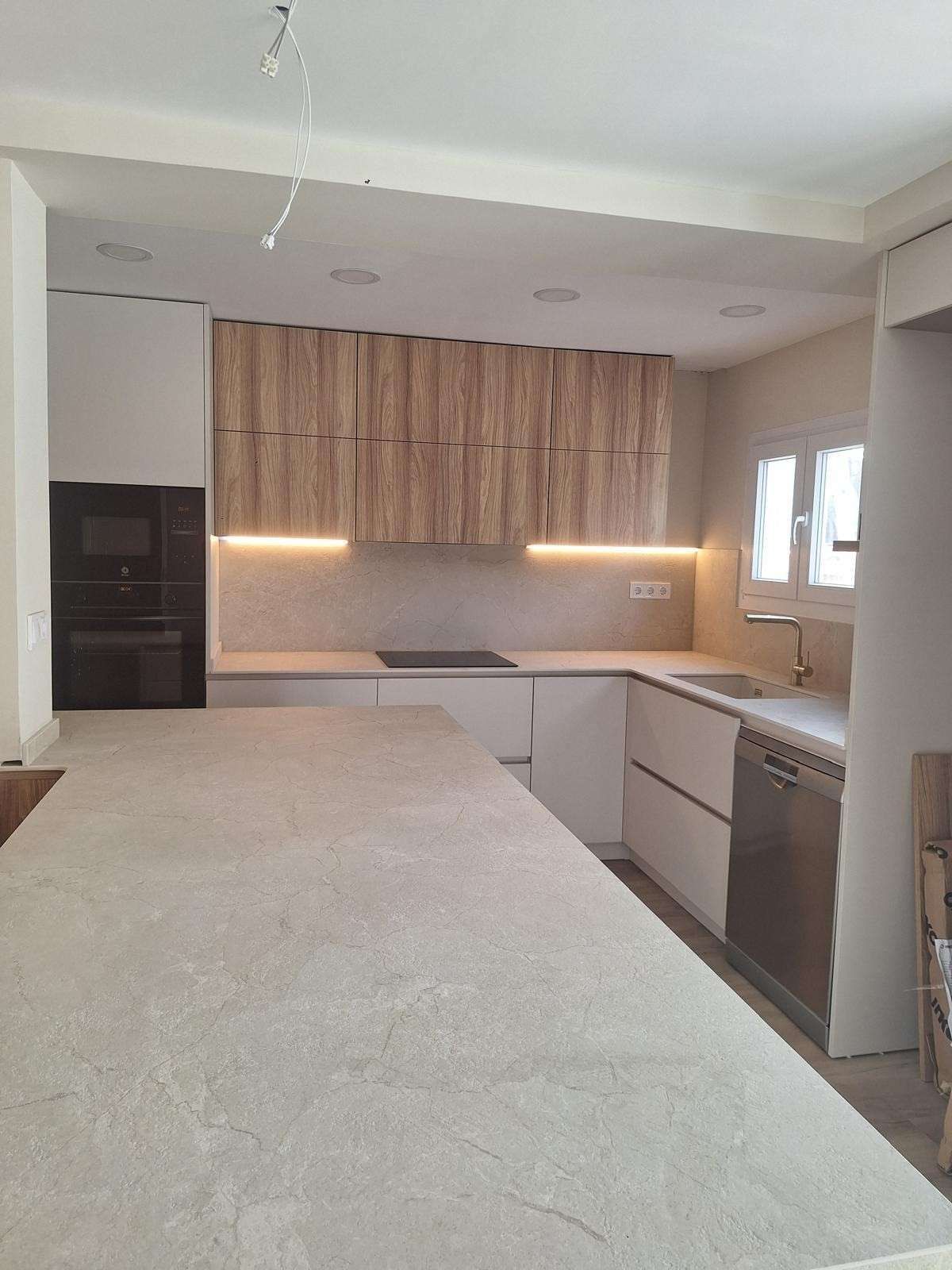 Cocina moderna blanca con gabinetes de madera, isla de piedra e iluminación debajo de los gabinetes.