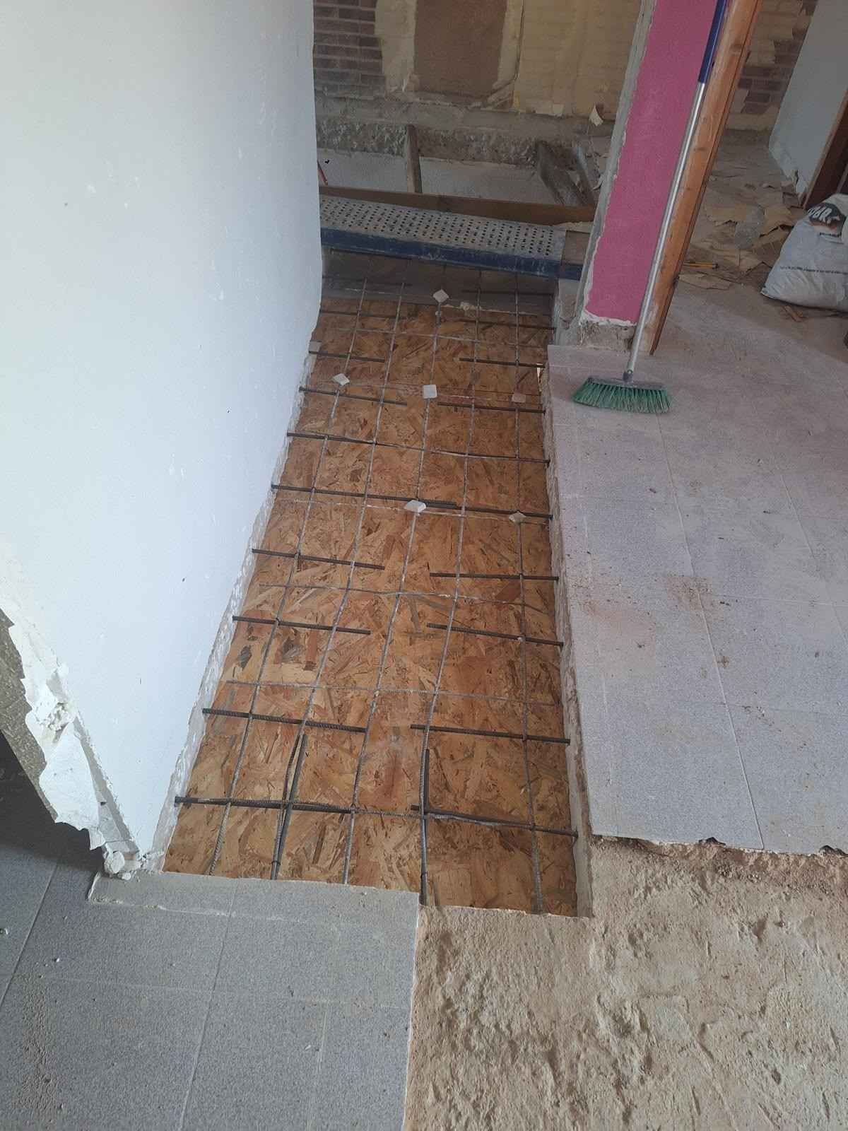 Parche de madera contrachapada expuesta en el subsuelo de una habitación en renovación, junto a un suelo de baldosas y una puerta.