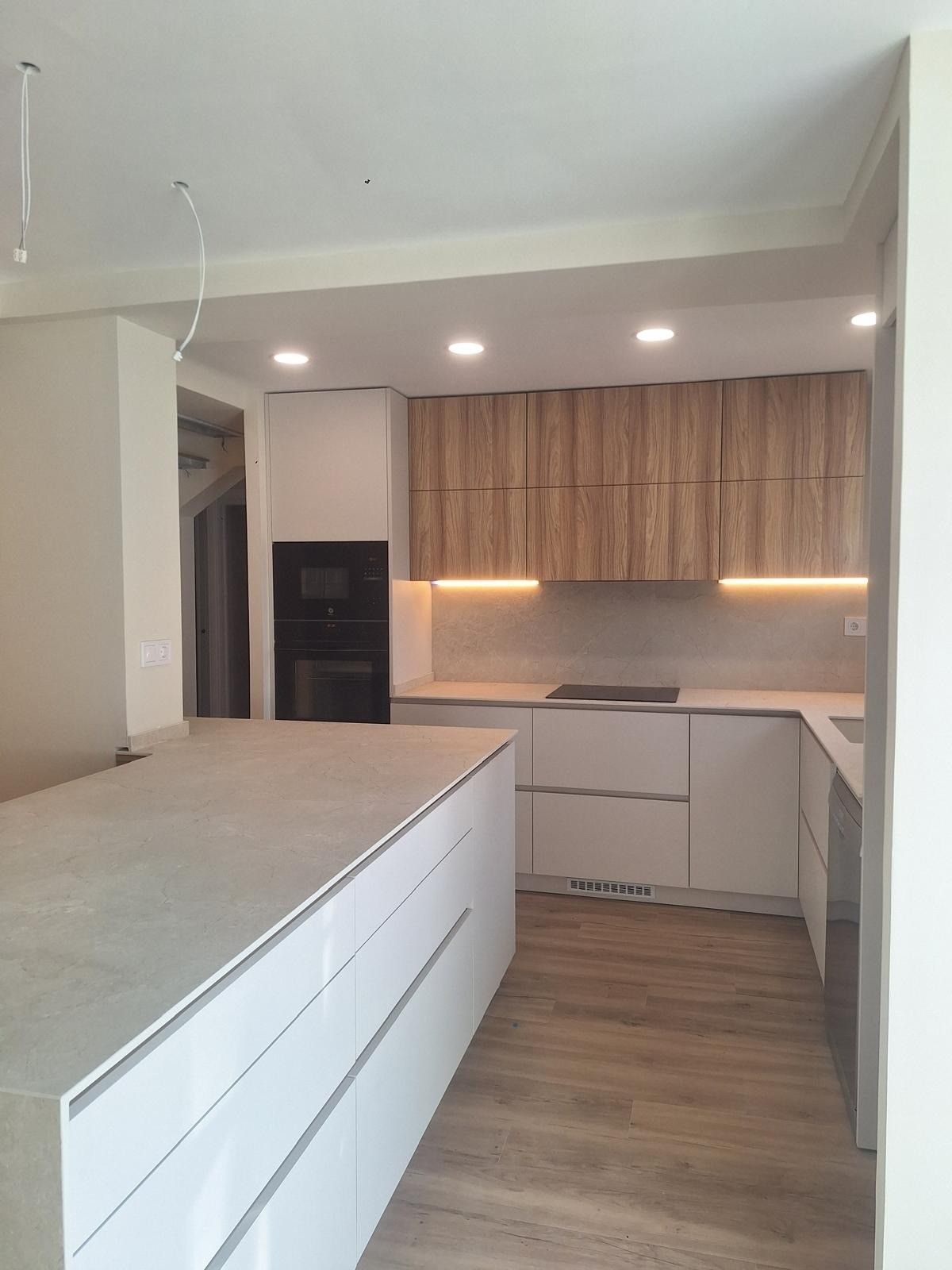 Cocina moderna con gabinetes de madera, isla blanca, iluminación cálida debajo de los gabinetes y piso con apariencia de madera.