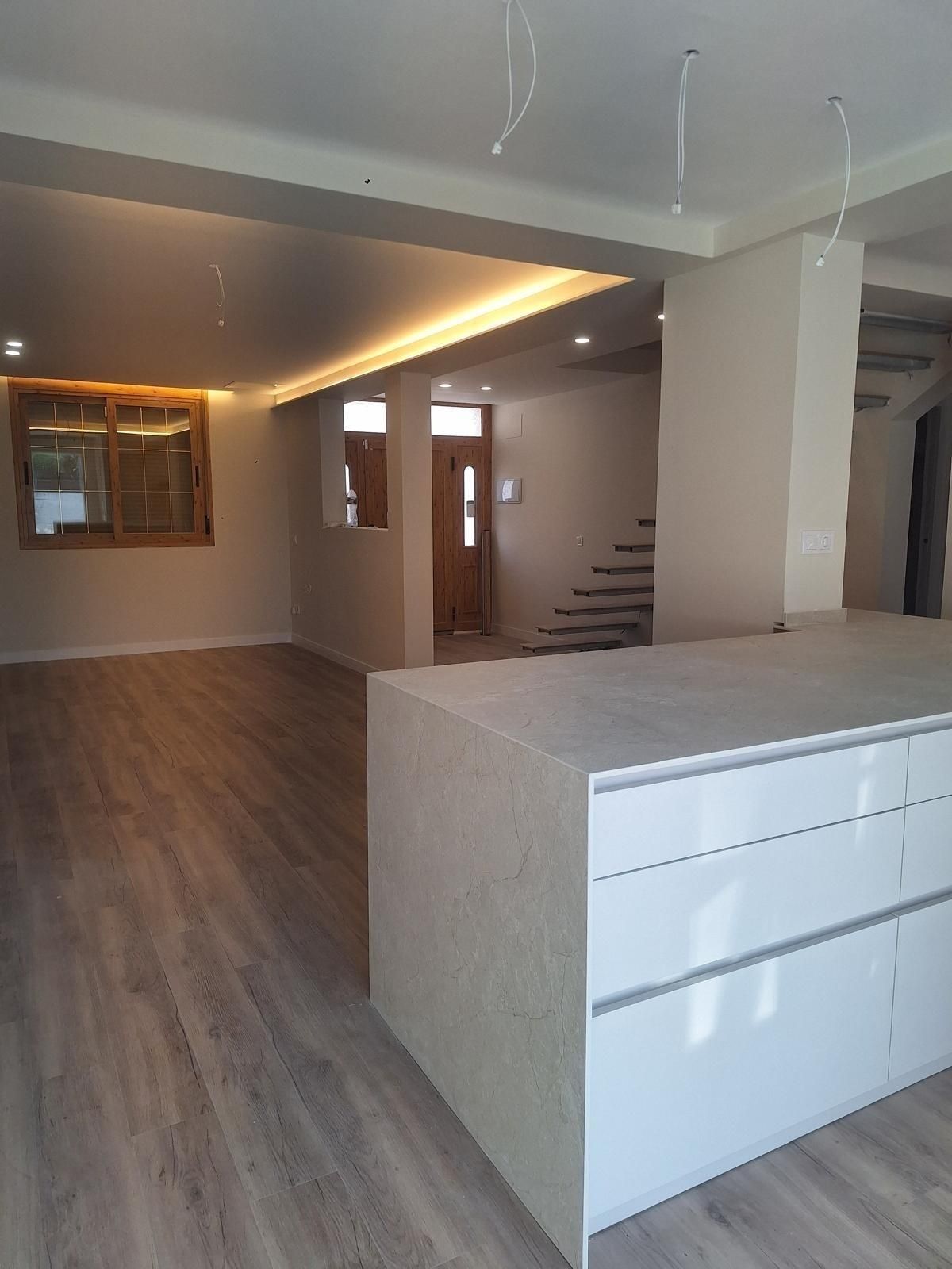 Espacio habitable moderno y vacío con suelo de madera, encimera blanca tipo isla y escalera abierta.