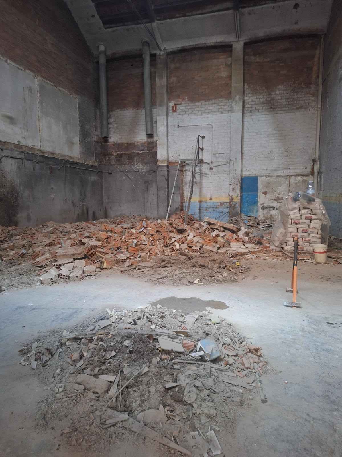 Obra en construcción interior con montones de escombros, paredes de ladrillo visto y suelo de hormigón.