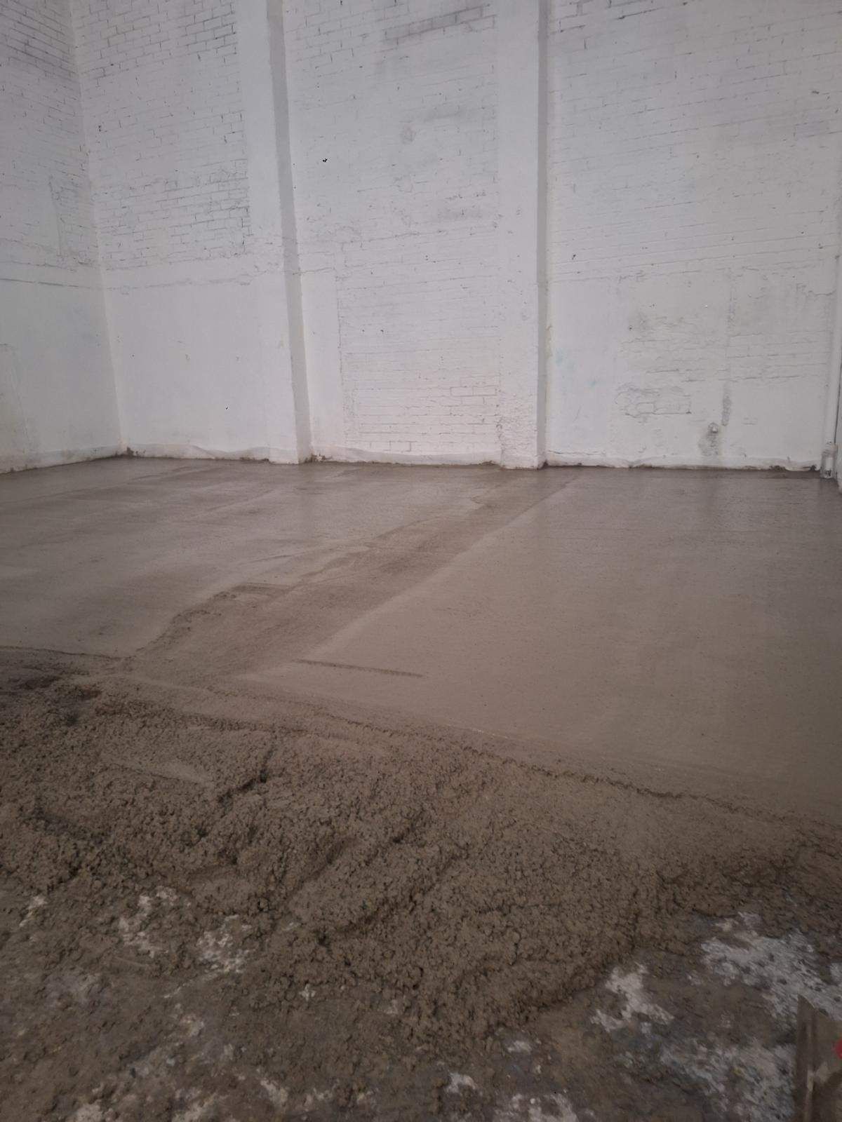 Suelo de hormigón recién vertido contra una pared blanca en la esquina de una habitación.