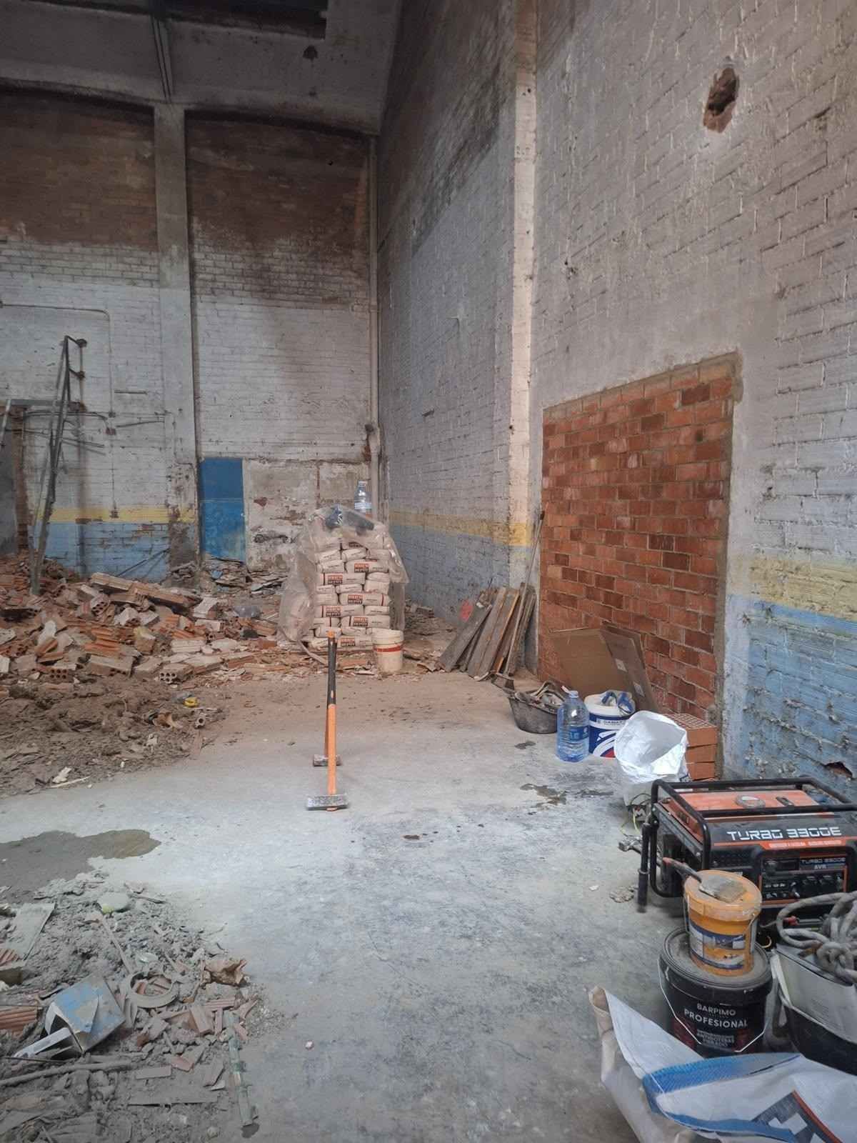 Interior de un almacén abandonado con escombros, paredes de ladrillo visto y materiales de construcción esparcidos por el suelo.