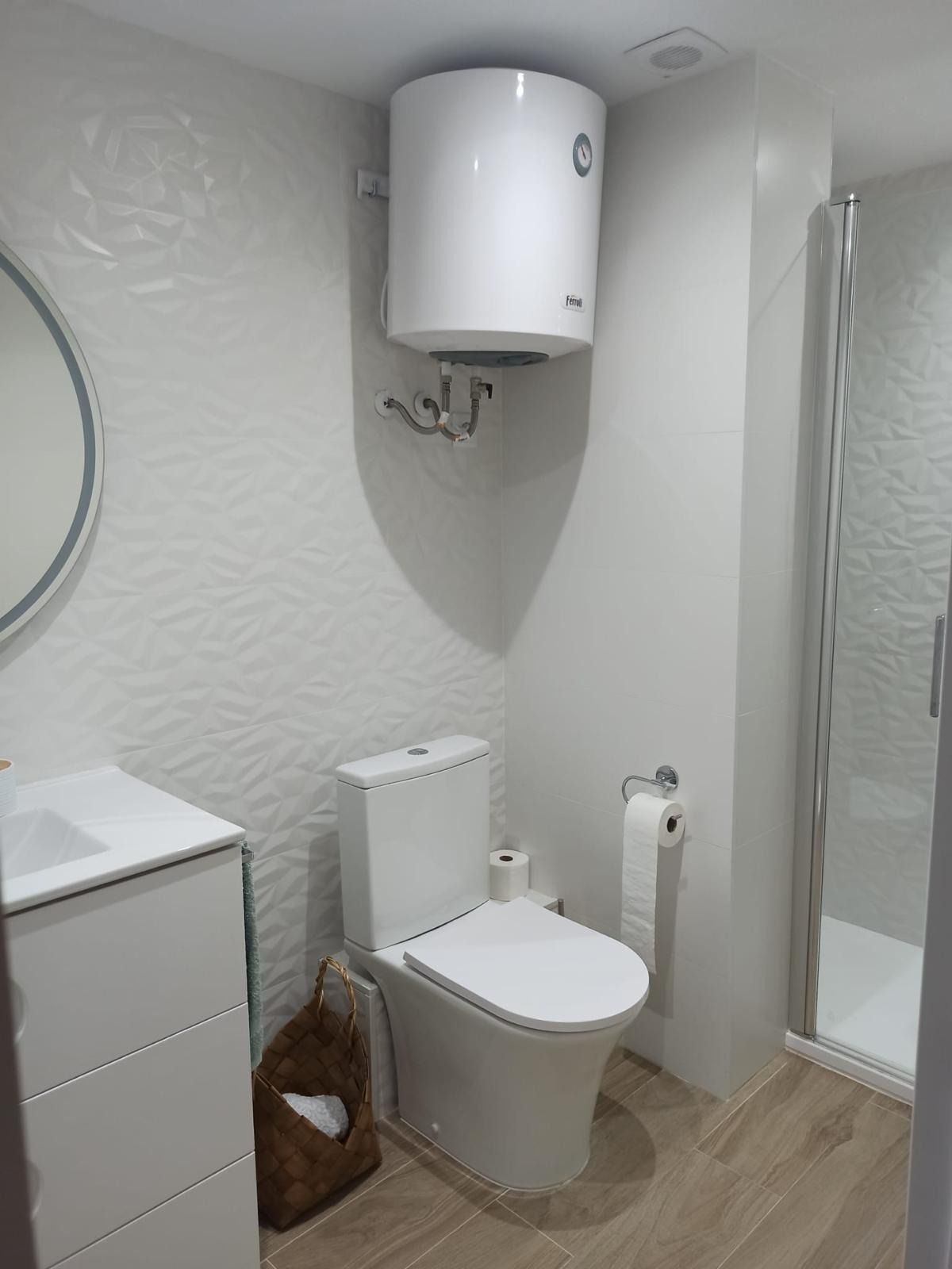 Baño pequeño y moderno con inodoro, calentador de agua mural, lavabo y cabina de ducha de cristal.