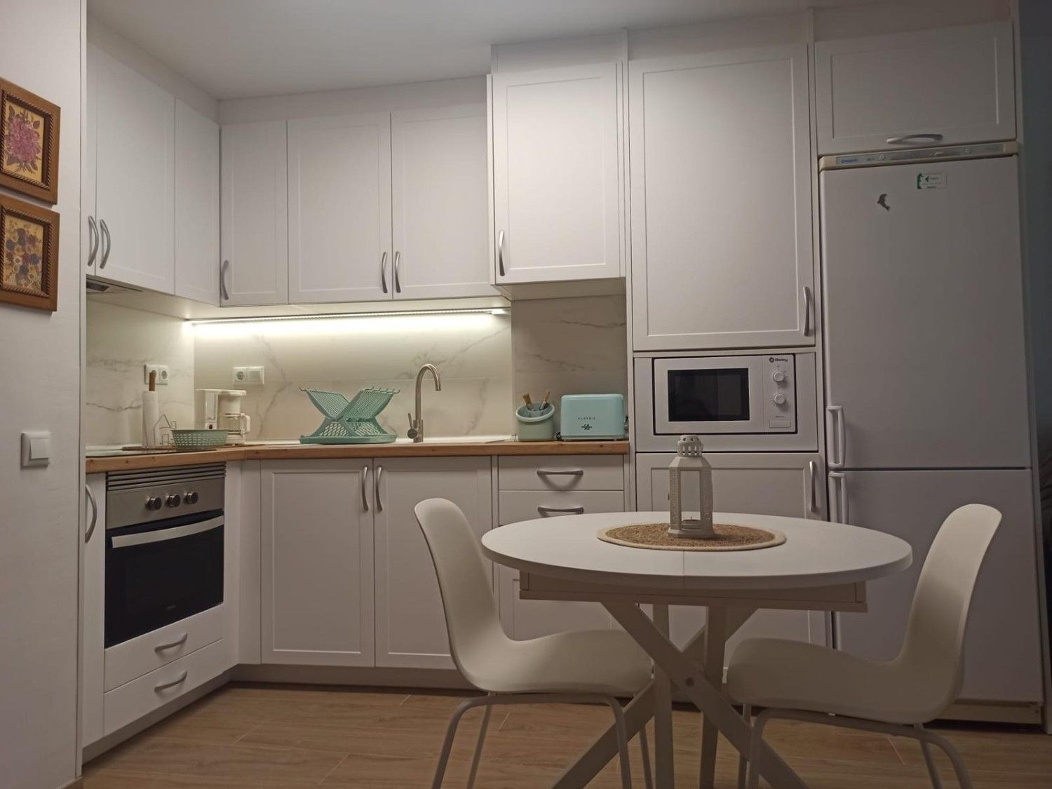 Cocina moderna de color blanco con electrodomésticos integrados y una mesa de comedor redonda junto a la pared.