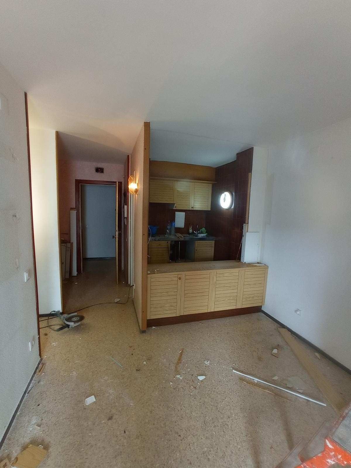 Pasillo de apartamento vacío con suelo de terrazo, paredes blancas y una pequeña cocina abierta al final.