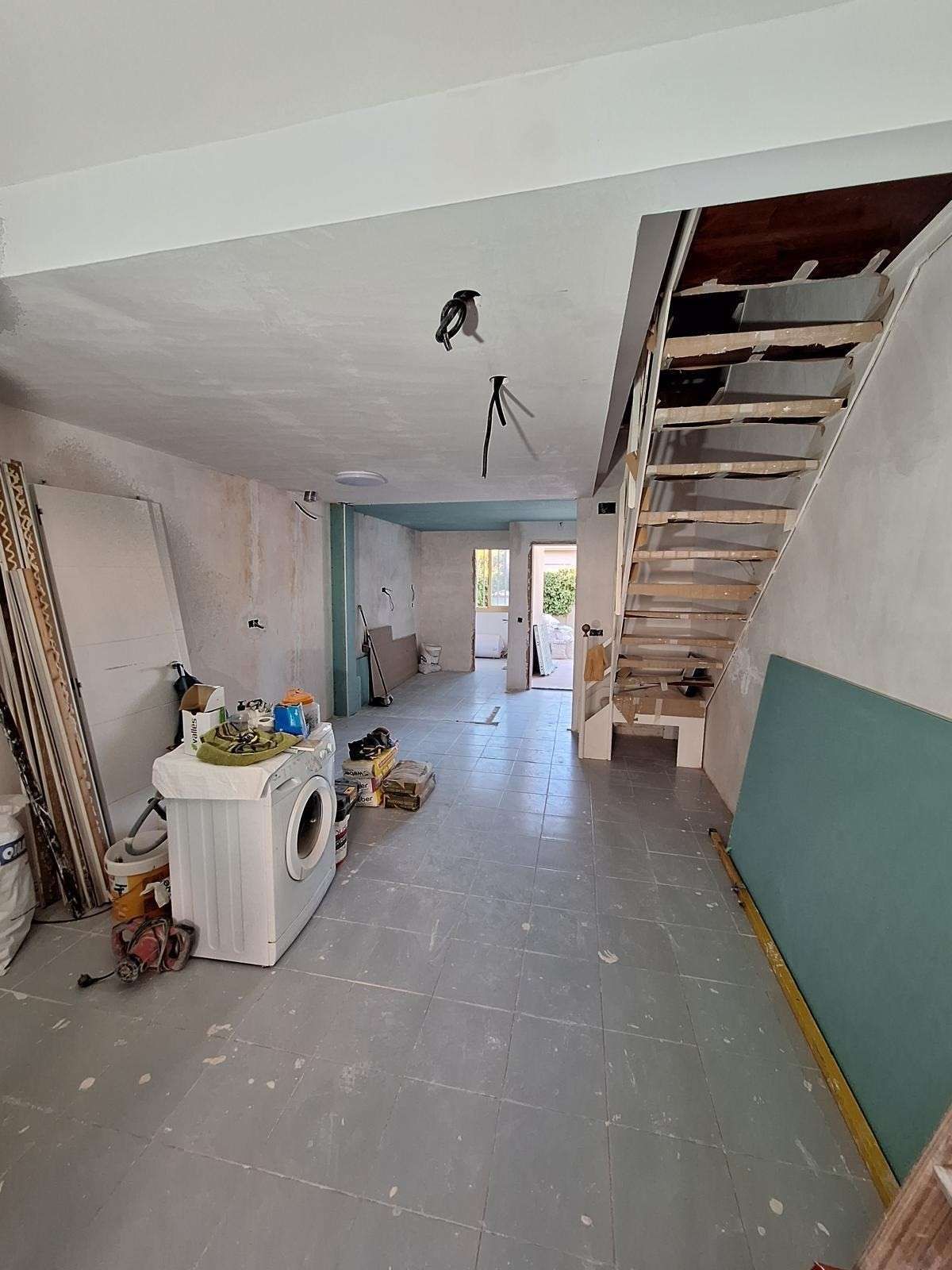 Cuarto de reforma con escaleras, lavadora, herramientas y paneles de pared verdes.