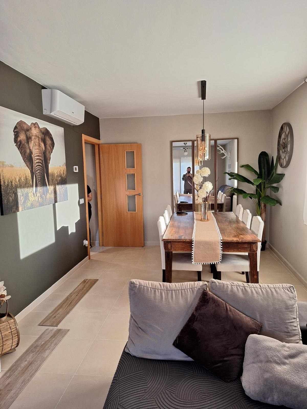 Salón-comedor moderno con cuadro de elefante en la pared, muebles beige y una mesa de madera cerca de una puerta de cristal.