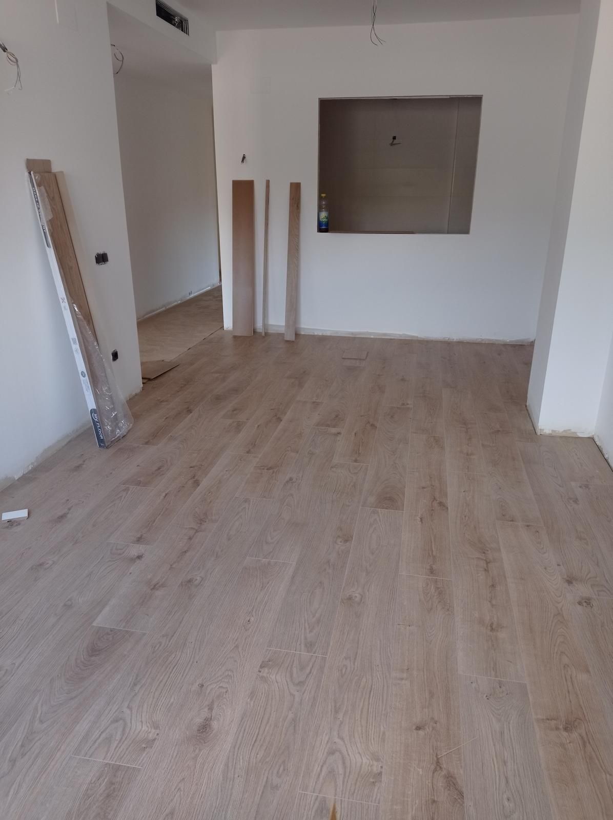 Habitación vacía con suelo de madera clara, paredes blancas y una pequeña ventana interior.