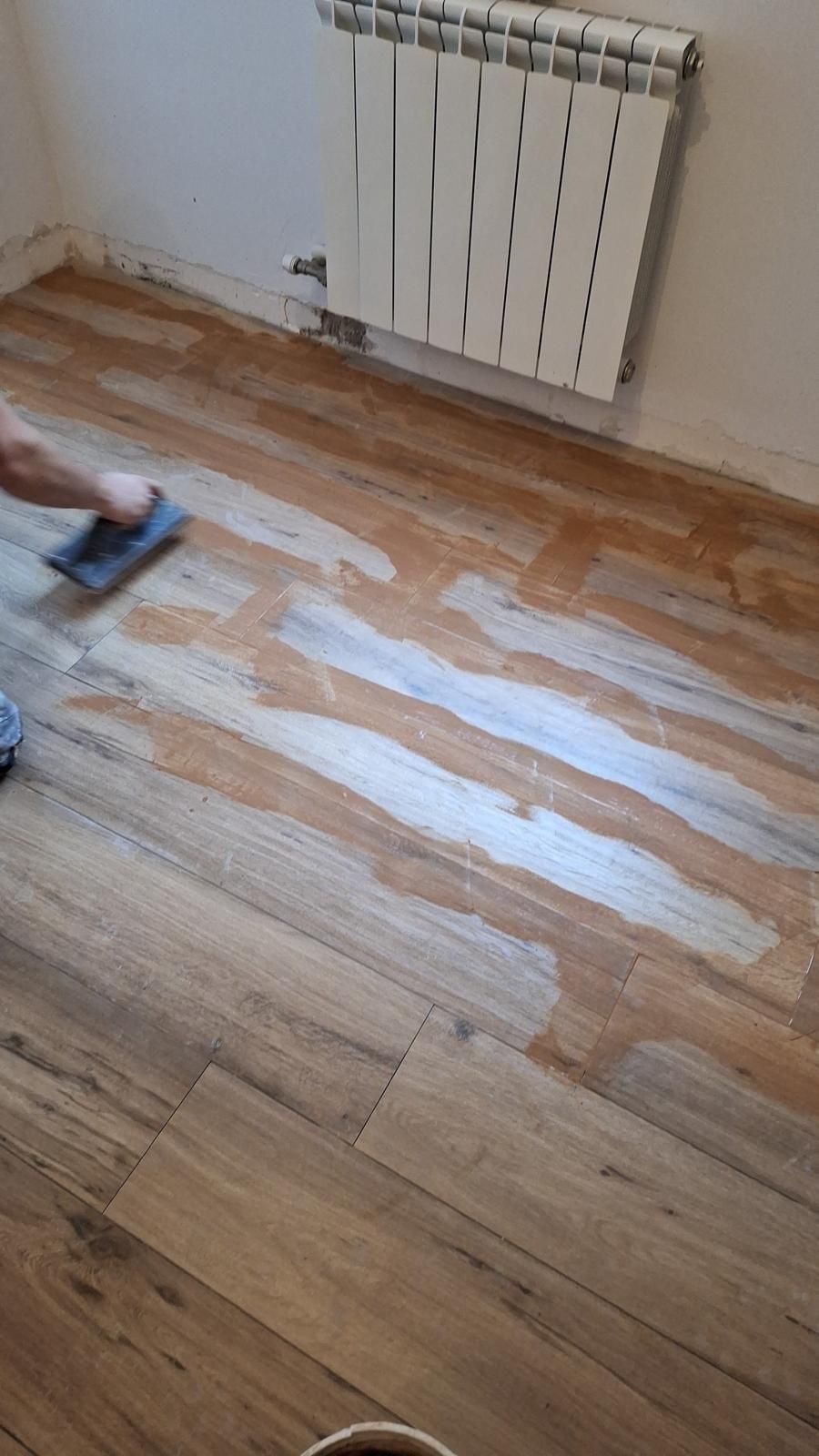 Suelo de madera lijado o restaurado, con un radiador en la pared encima.