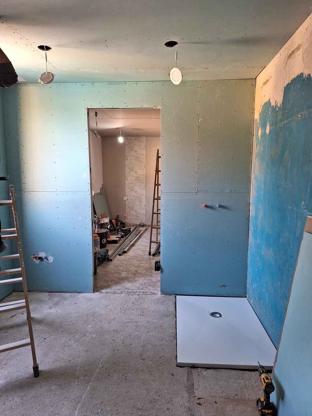 Habitación vacía en obras, con paredes azules, bombillas a la vista y escombros en el suelo.