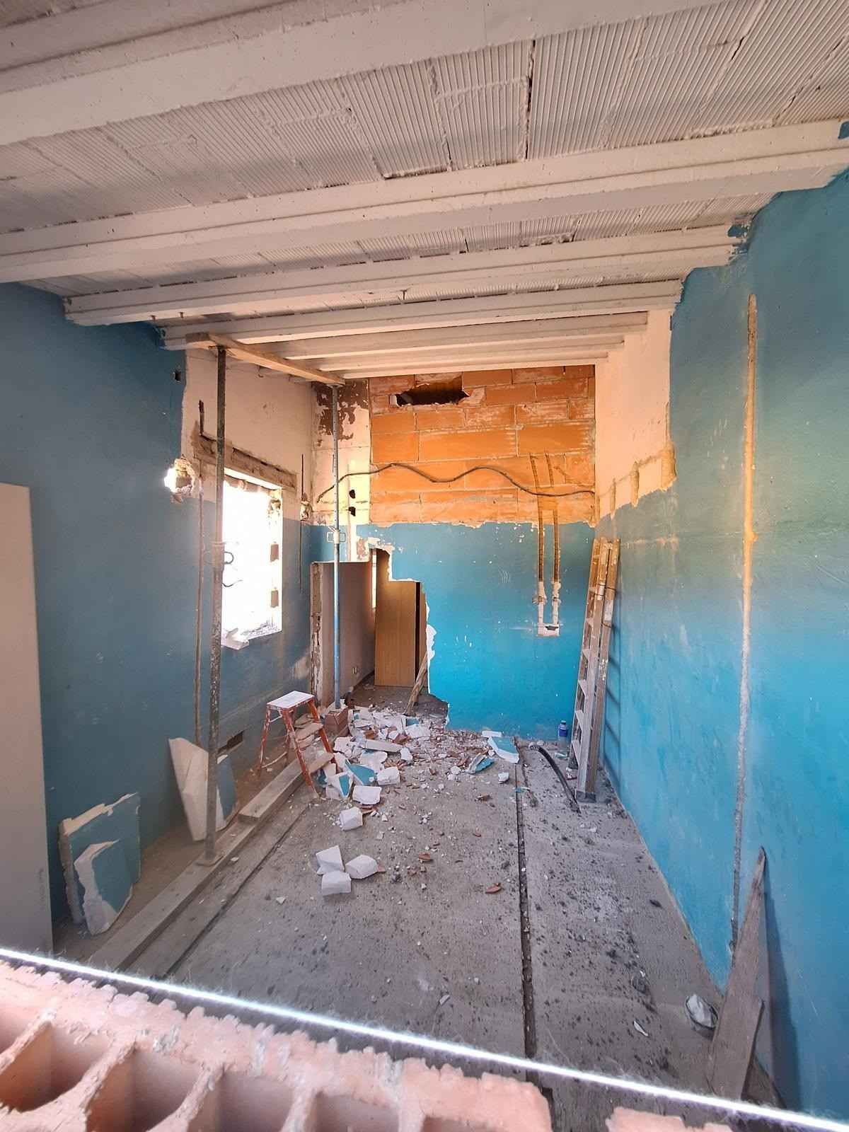 Habitación parcialmente demolida con paredes azules, escombros en el suelo y vigas expuestas en el techo.