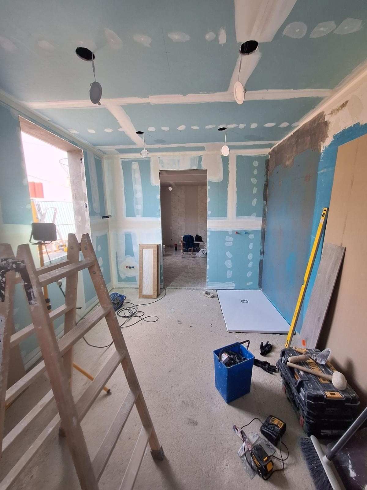 Habitación en obras con paredes azules, parches de pladur, escaleras, herramientas y escombros en el suelo.