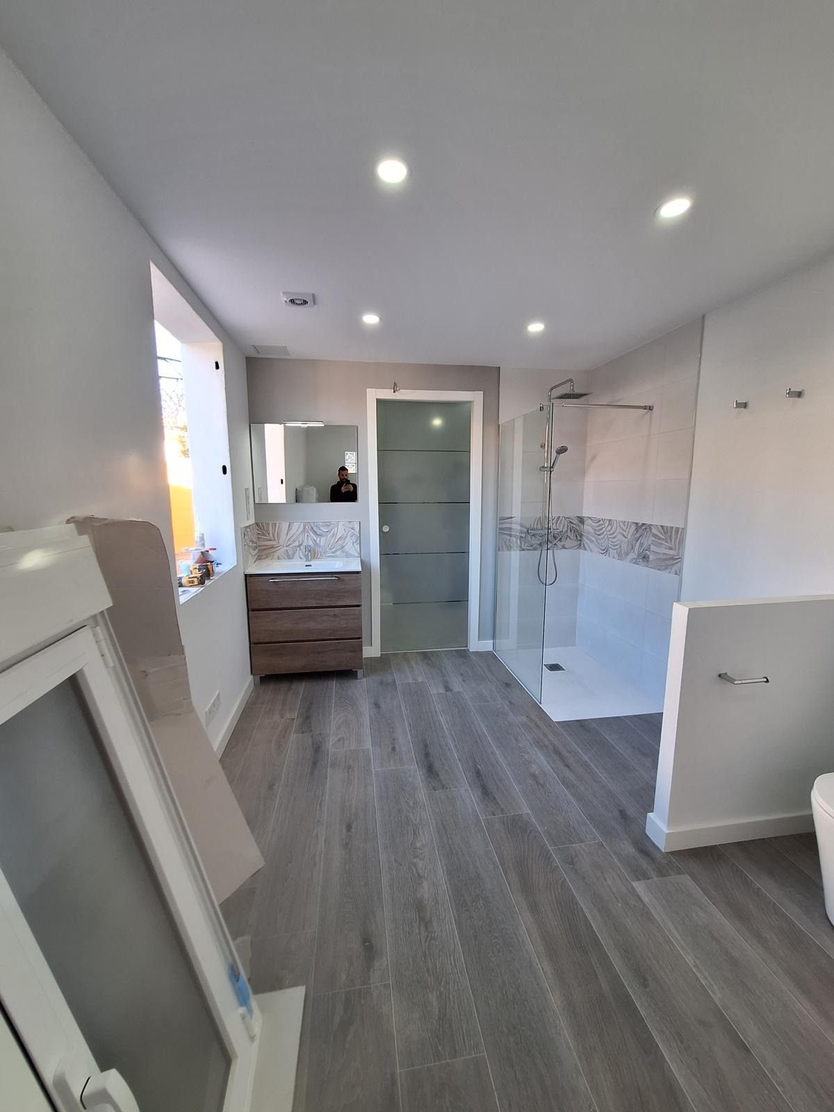 Baño moderno con suelo de baldosas grises, ducha a ras de suelo, tocador y paredes blancas.