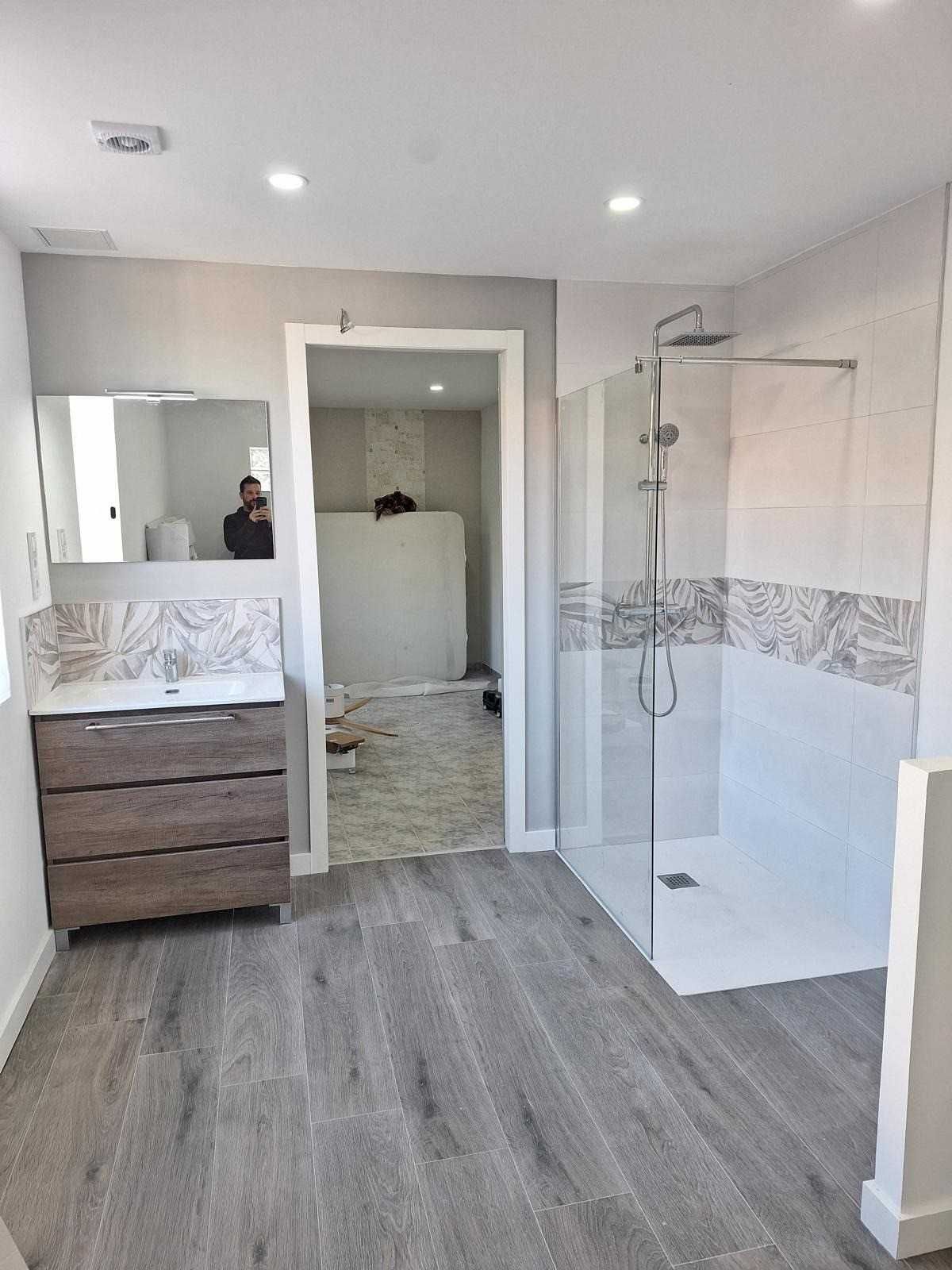 Baño moderno con ducha a ras de suelo, lavabo doble y suelo de imitación madera gris.