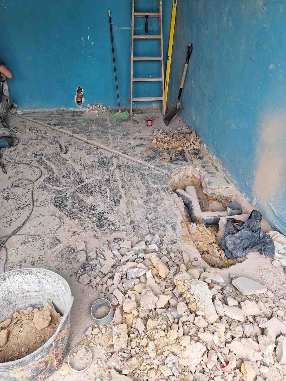 Habitación con paredes azules en proceso de renovación, con escombros en el suelo, una escalera y tuberías a la vista.
