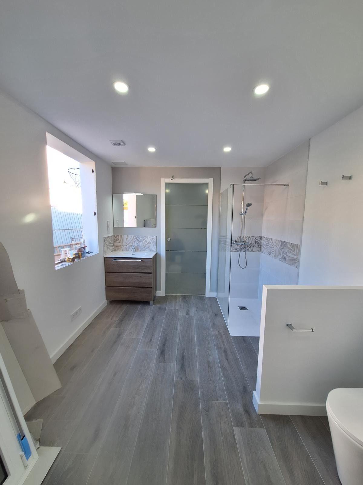 Baño moderno con ducha a ras de suelo, lavabo, inodoro y suelo gris bajo luces empotradas.