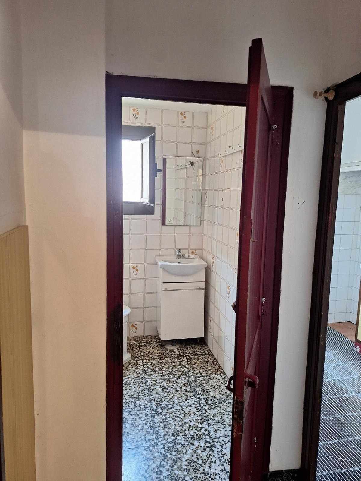 Pequeño baño con azulejos, lavabo, ventana y puerta granate abierta.