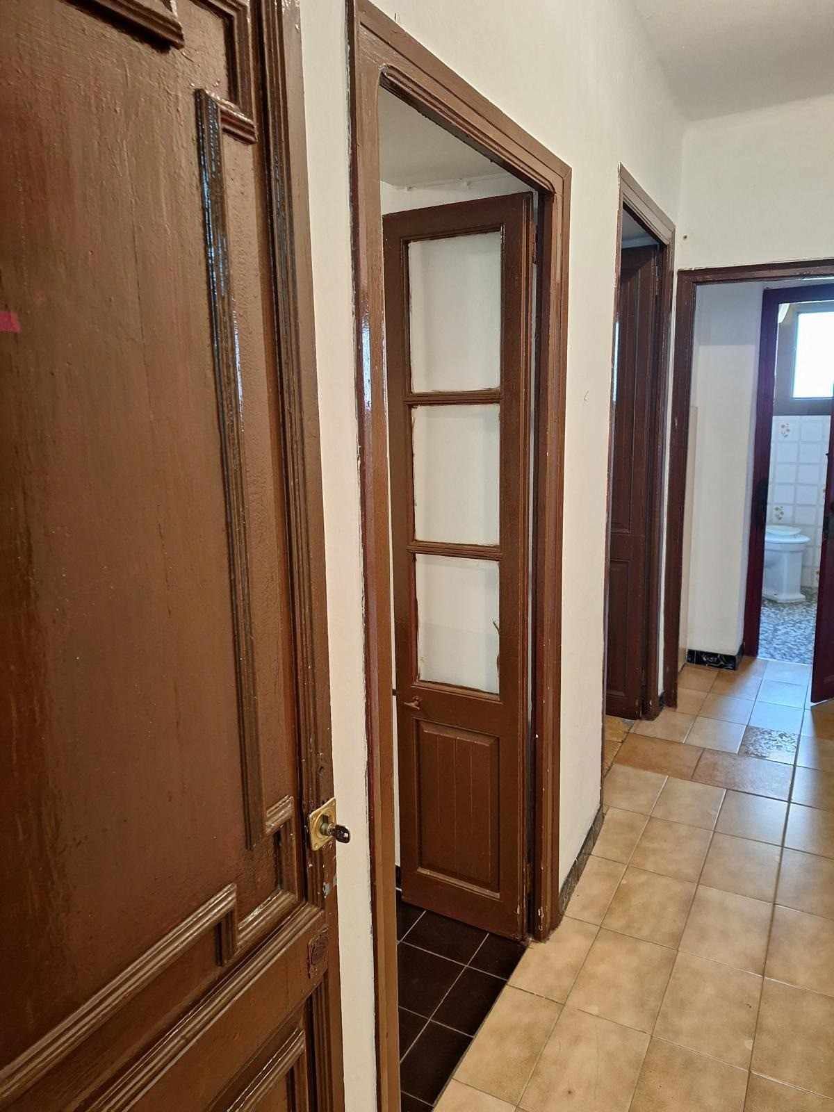 Pasillo con puertas de madera y suelo de baldosas en un interior residencial.
