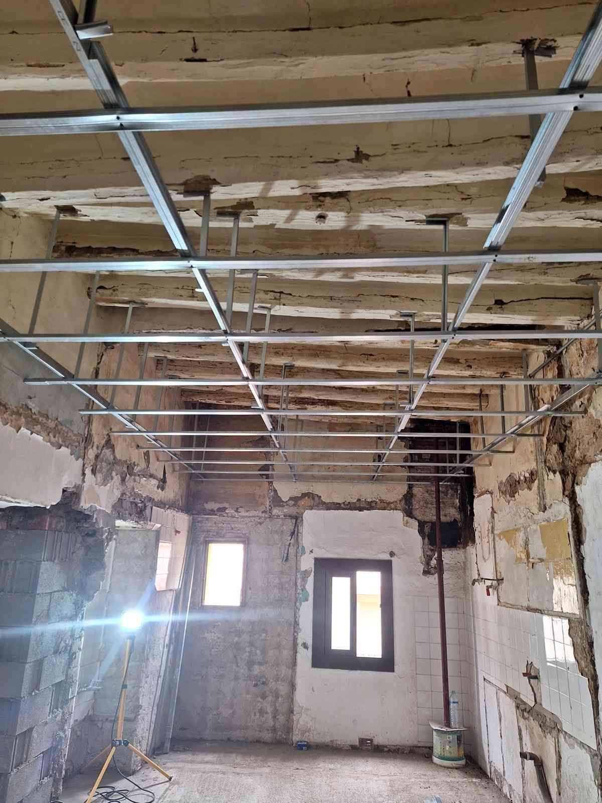 Habitación parcialmente reformada con vigas de techo a la vista, conductos de ventilación colgantes y dos ventanas pequeñas.