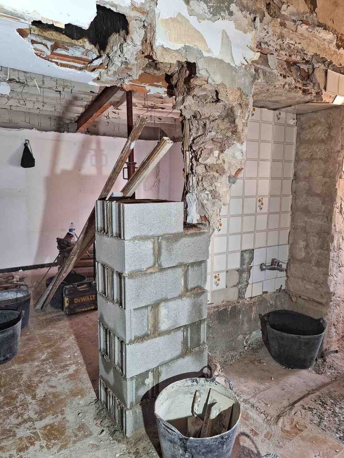 Interior parcialmente demolido con escombros, vigas de techo a la vista y un tabique de bloques de hormigón en construcción.