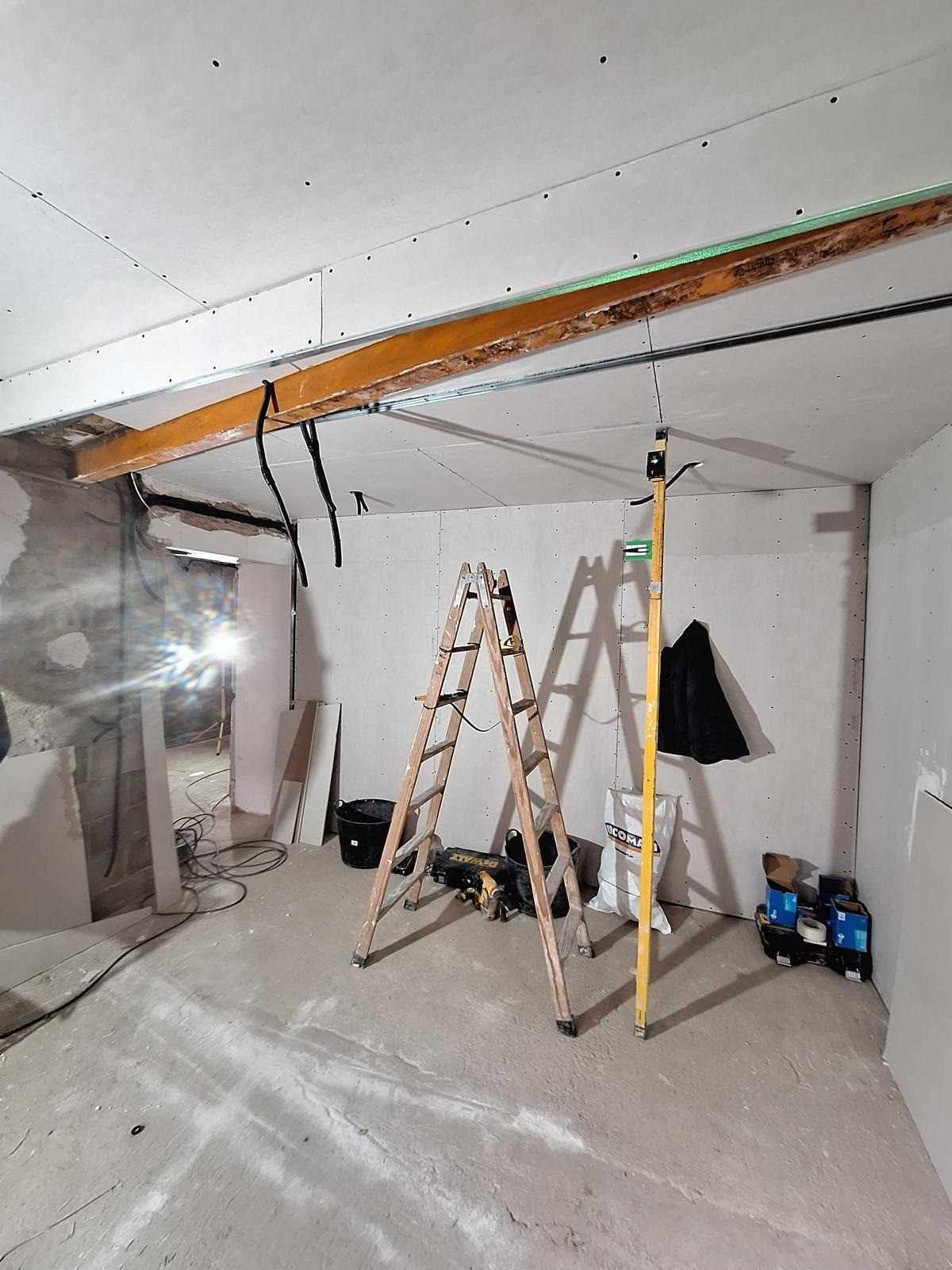 Habitación parcialmente reformada con escaleras, herramientas y vigas de techo a la vista.