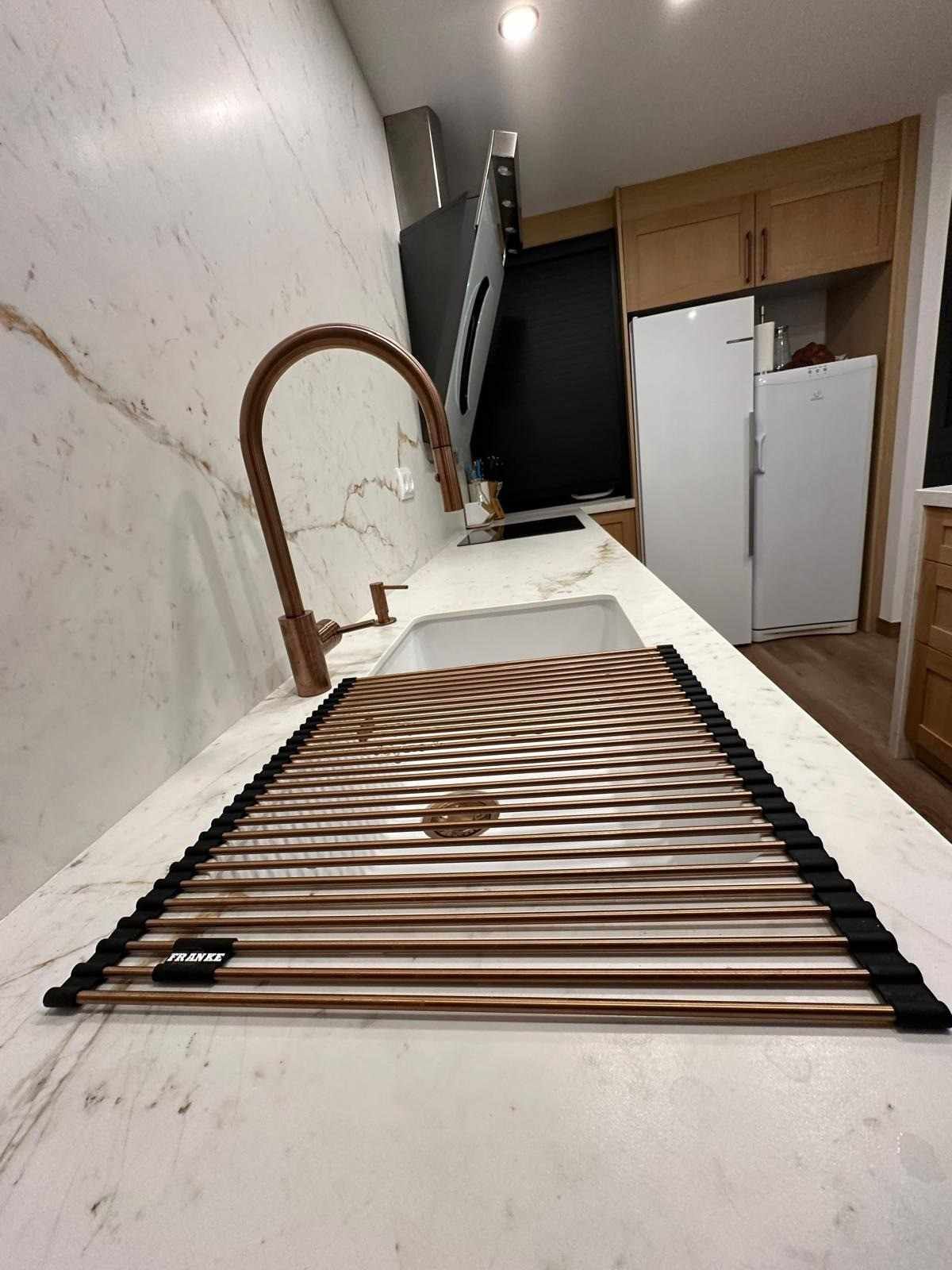 Fregadero de cocina con alfombrilla a rayas, grifo de cobre, armarios blancos y un pasillo estrecho detrás.