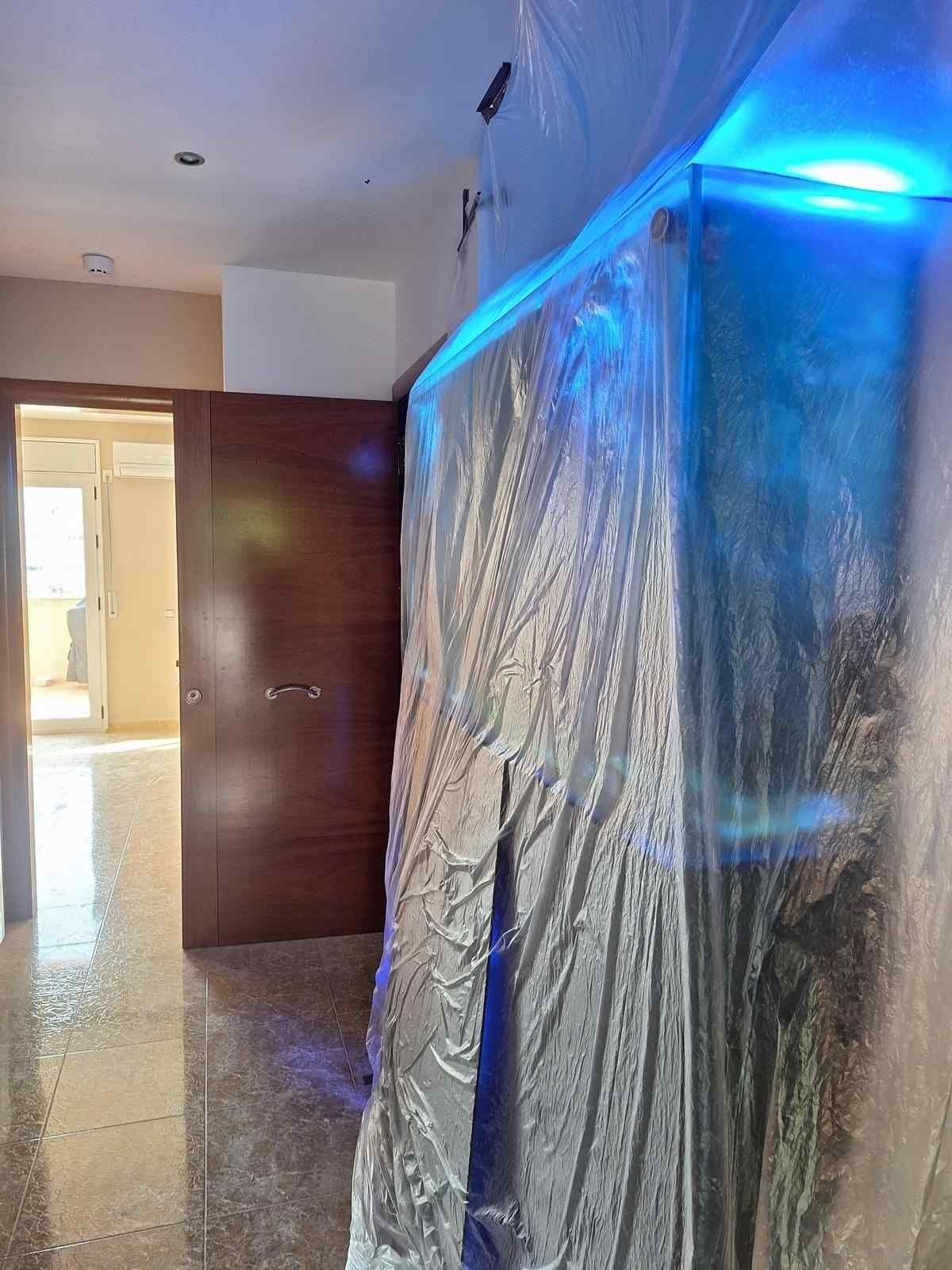 Pasillo con una gran pared cubierta de plástico iluminada con luz LED azul, junto a una puerta de madera abierta.