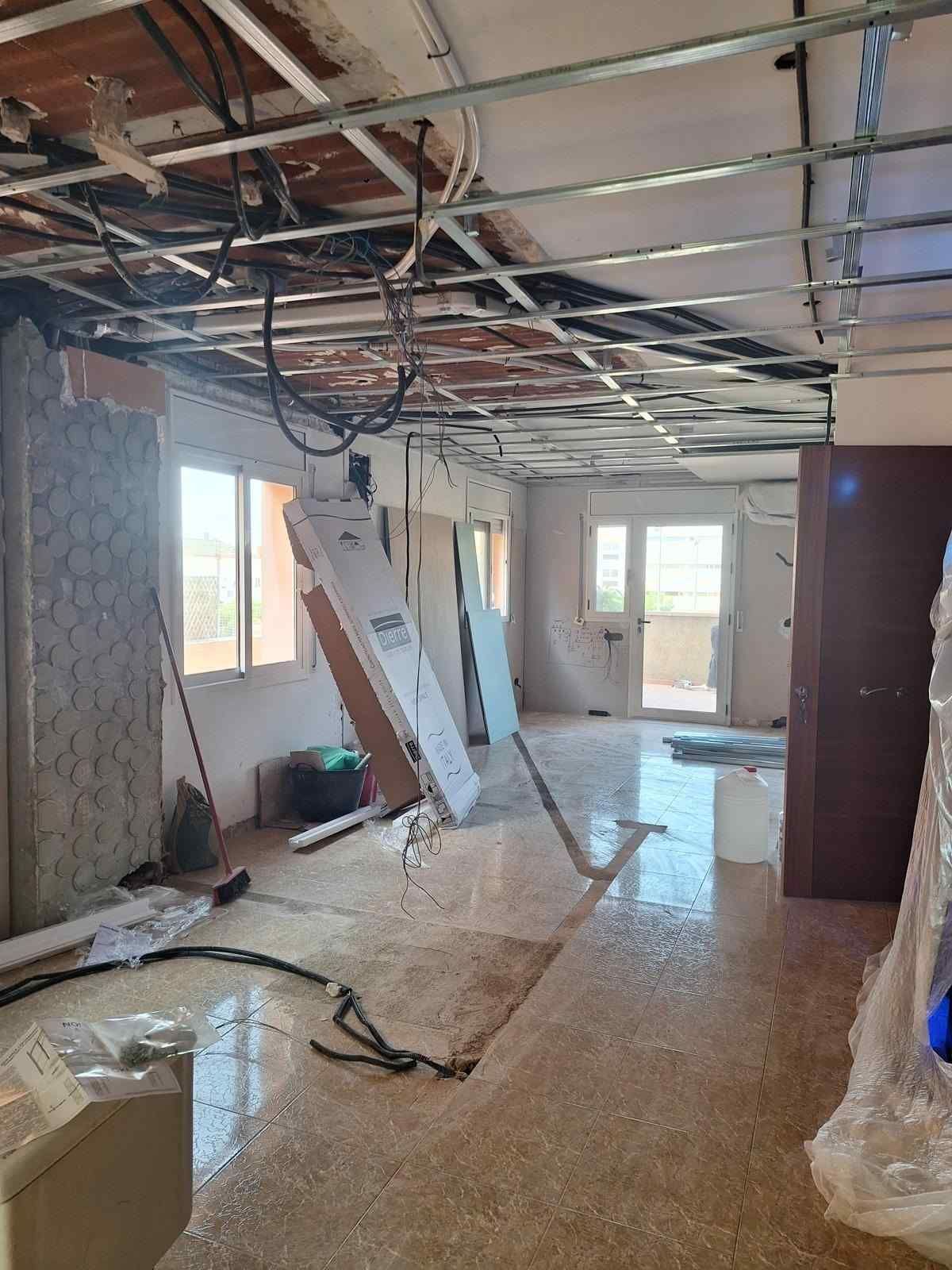 Interior de la habitación dañado con techo expuesto, escombros y materiales de construcción durante la renovación.