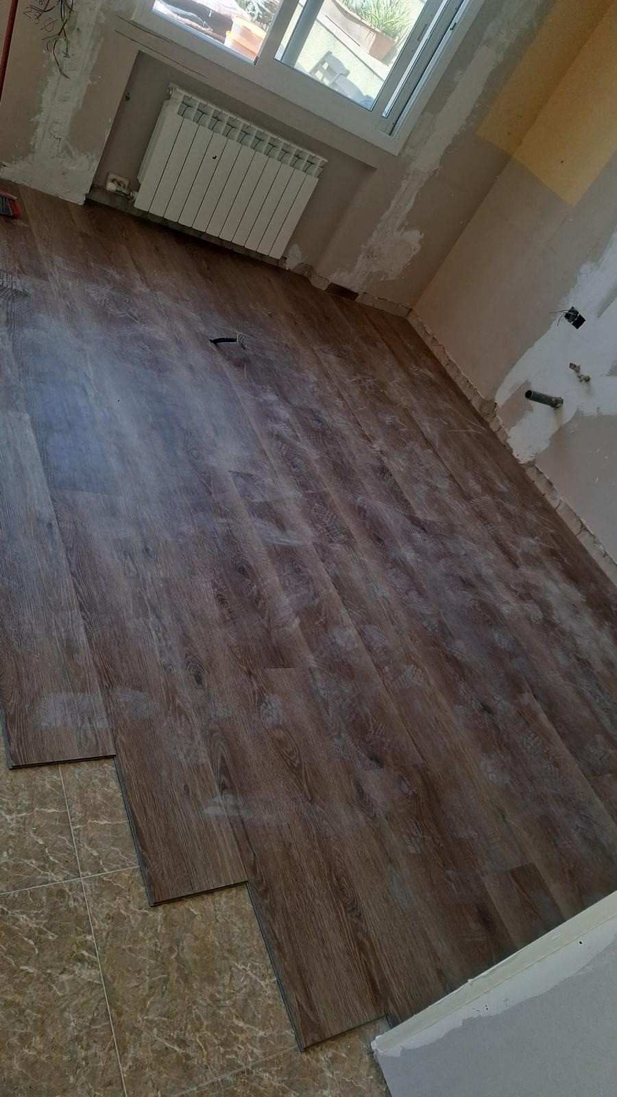 Habitación vacía con suelo de imitación madera, una ventana, un radiador y paredes blancas.
