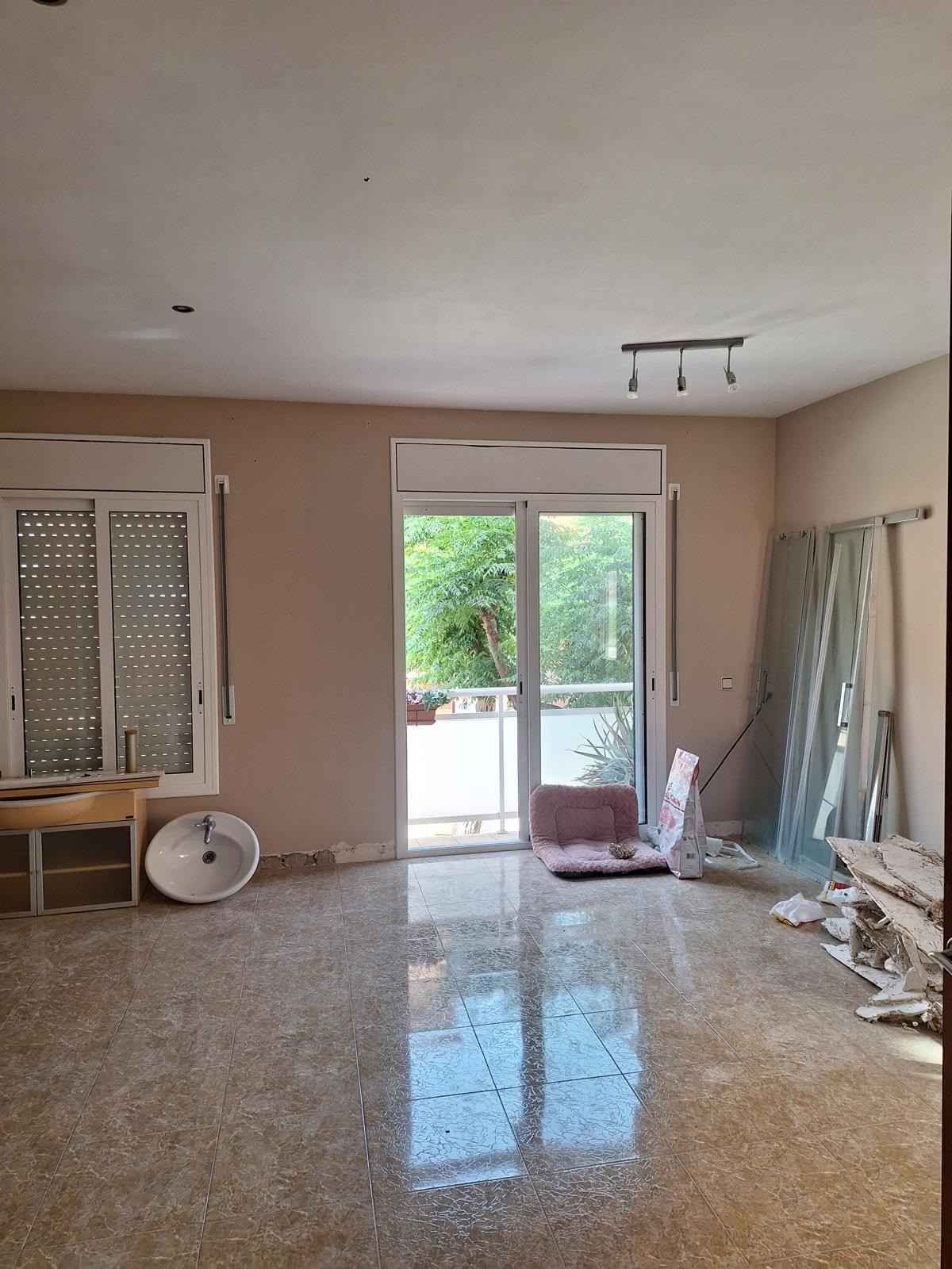 Sala de estar vacía con suelo de baldosas brillantes, puerta corredera de cristal y objetos apilados a lo largo de la pared derecha.