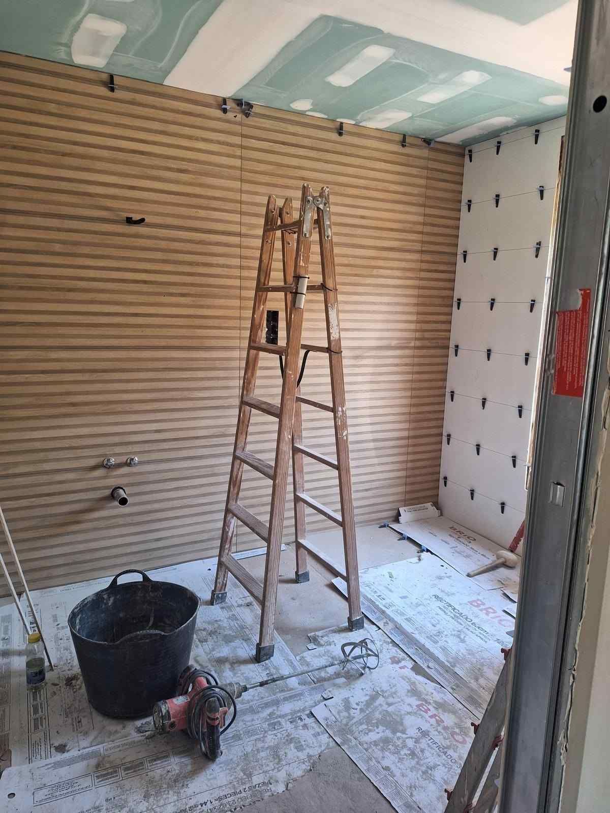 Cuarto de reformas con escalera, cubo y herramientas en un suelo polvoriento junto a paredes sin terminar.