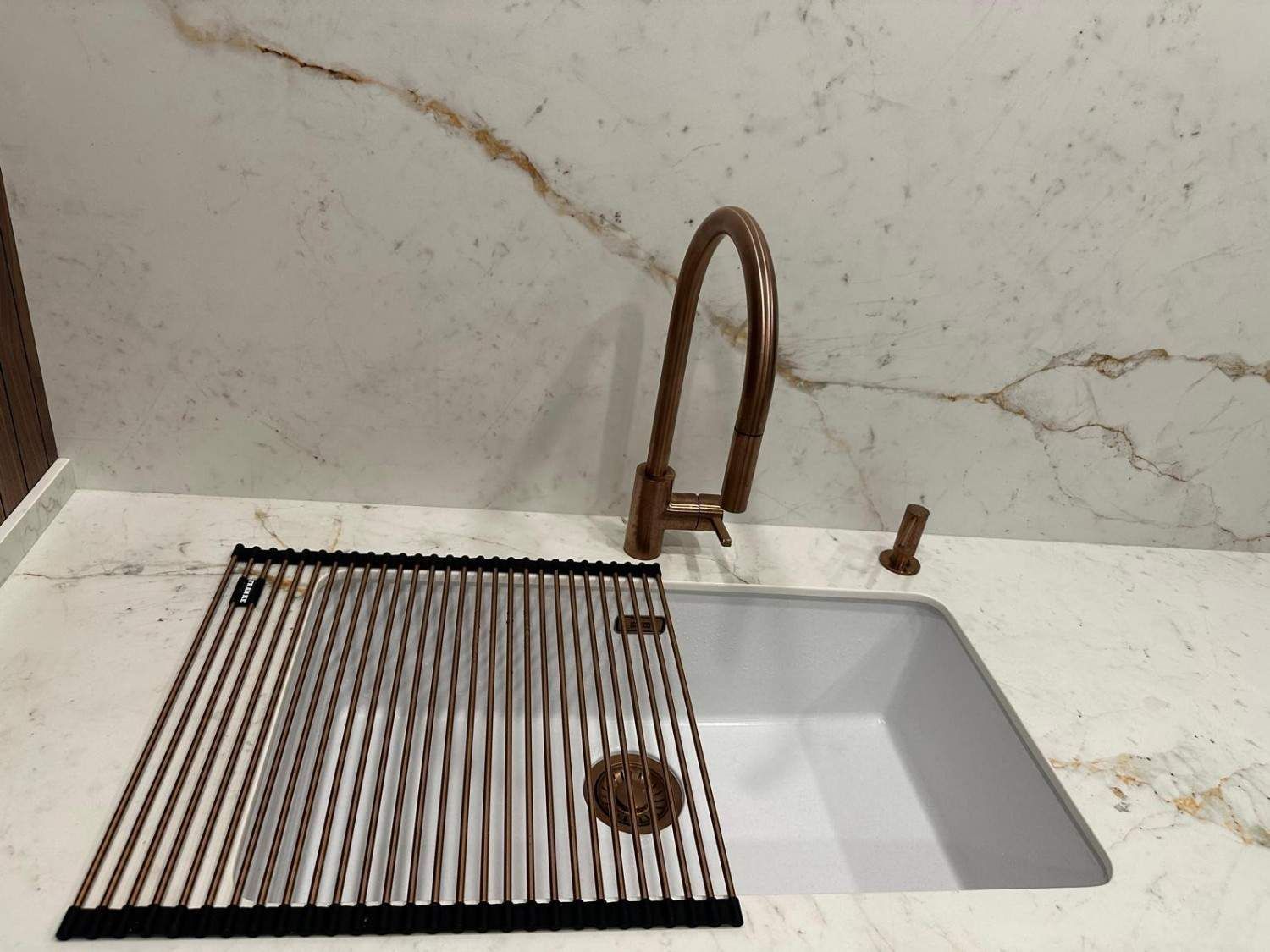 Fregadero de cocina con un escurridor de platos de listones negros sobre la encimera y un grifo curvo sobre un lavabo blanco.