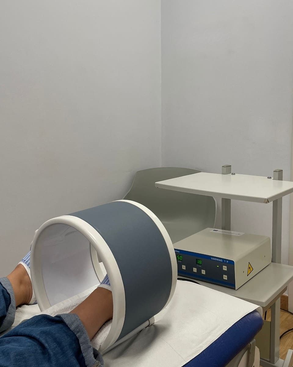 Persona recibiendo magnetoterapia, con las piernas dentro de un dispositivo circular. Equipo médico en un entorno clínico.