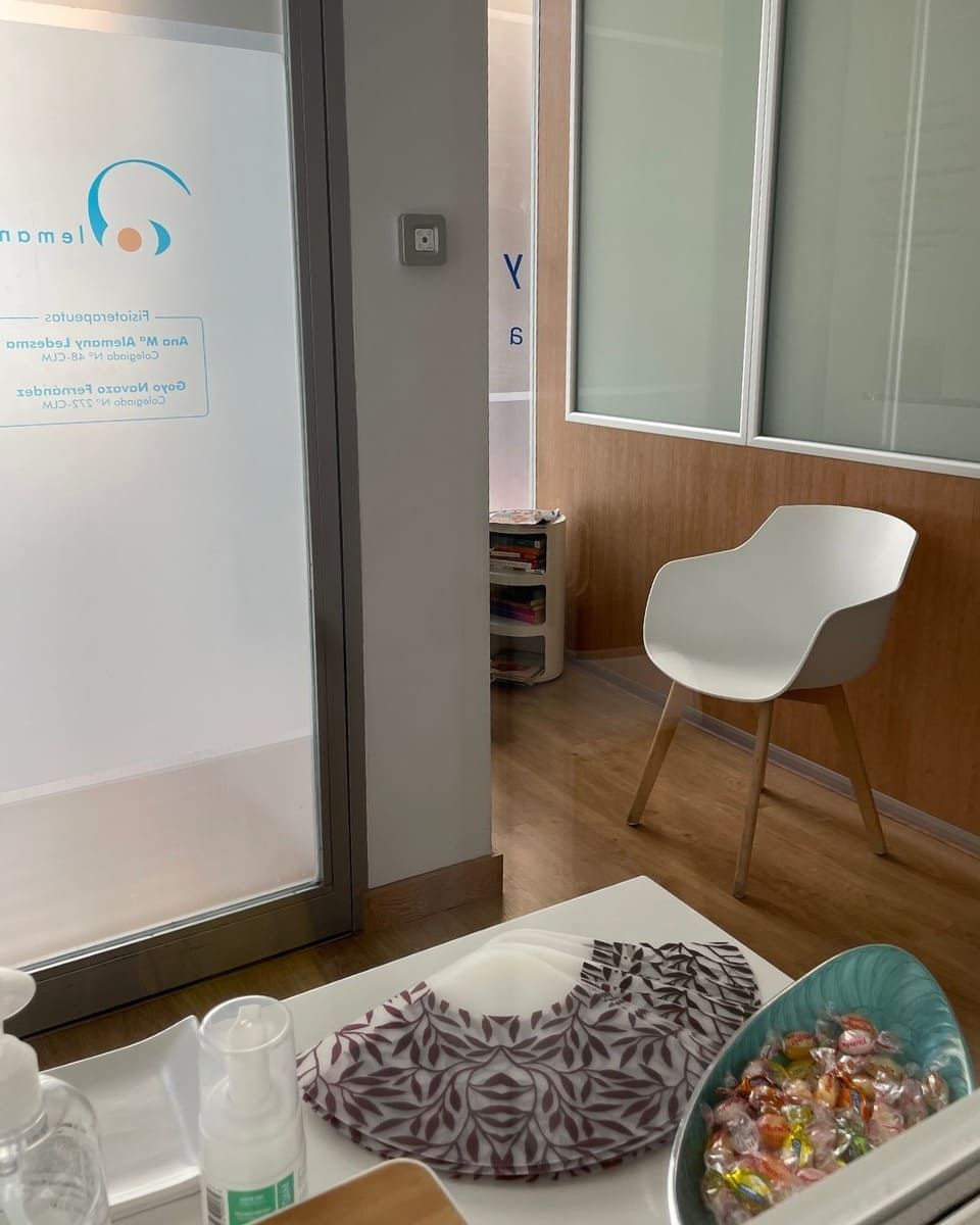 Una sala de espera con una silla, una puerta de cristal y un bol de dulces. Cubrepiés y otros productos sobre una mesa.