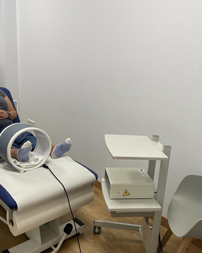 Habitación clínica con sillón reclinable, dispositivo de luz anular y equipo médico en un carrito.