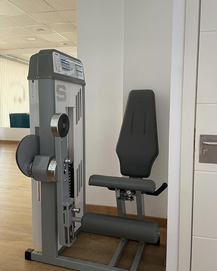 Máquina de ejercicios sentada en un gimnasio, de color gris y negro, con respaldo y asiento acolchados.