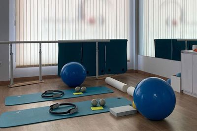Suelo de gimnasio con balones de ejercicio azules, pesas, colchonetas y bandas de resistencia en una habitación luminosa.