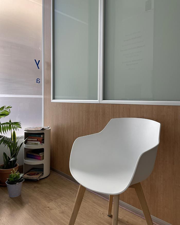 Rincón de oficina moderno con una silla blanca, paneles de madera, ventana esmerilada y pequeñas plantas.
