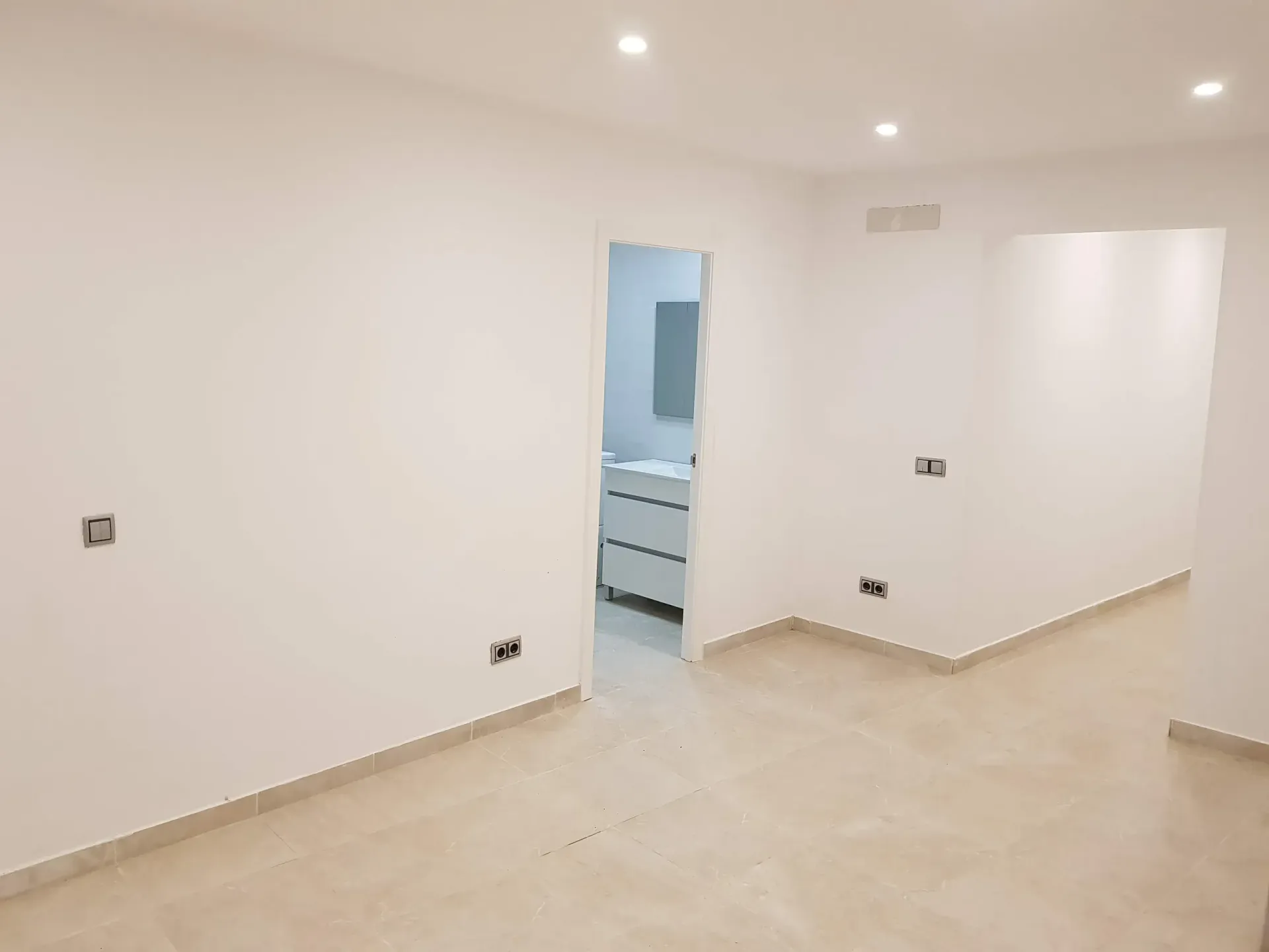 Una habitación vacía con paredes blancas y una puerta que conduce a un baño.