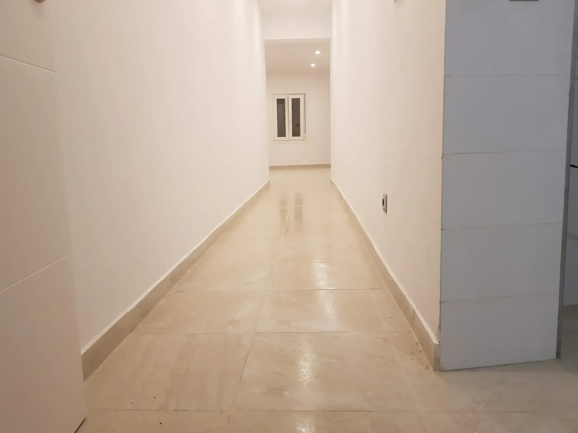 Un pasillo largo con paredes blancas y pisos de baldosas en un edificio.