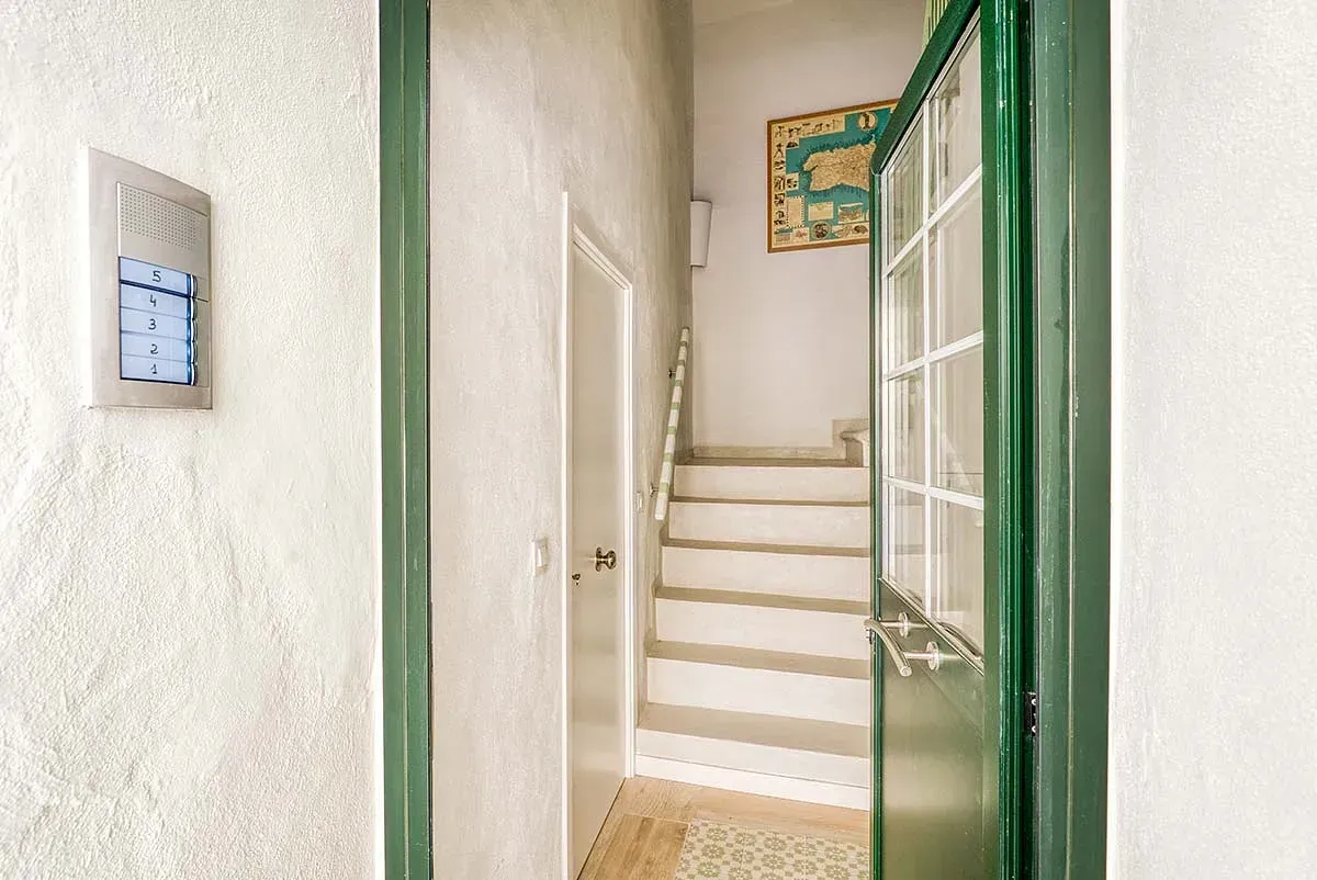 Un pasillo con escaleras blancas y una puerta verde que conduce al segundo piso.