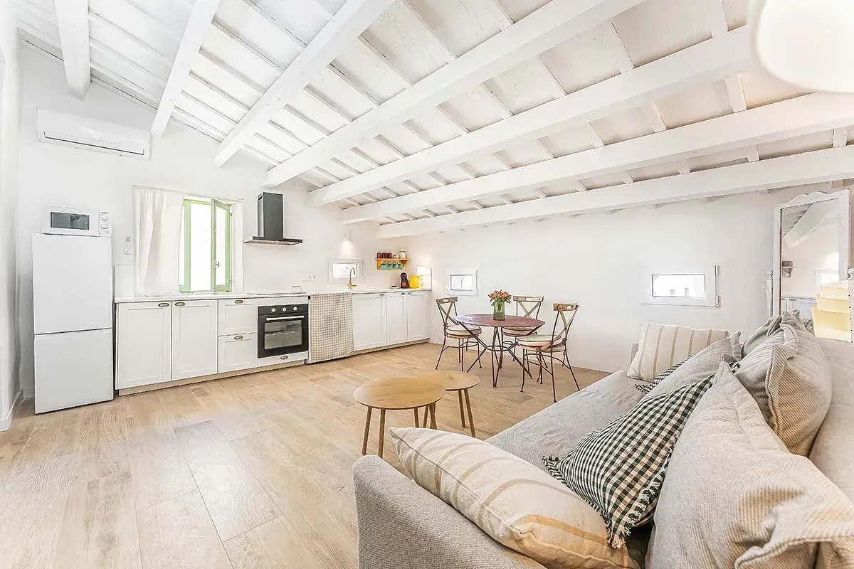Una sala de estar con sofá, mesa y sillas y una cocina.